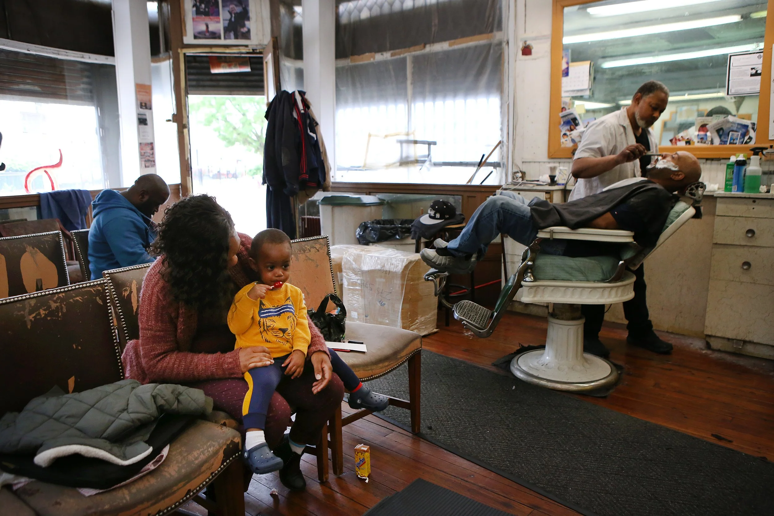  Shantel Burno waits with her son, Ryan Broadway, 1, for his haircut at a barbershop on the corner of Ocean Avenue and Grant Avenue in Jersey City, New Jersey. (Erica Lee for The Wall Street Journal) 