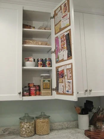 Cork tiles inside a kitchen cabinet.  Clear the counter clutter (say that three times fast) and make recipes and shopping lists easily accessible.  Genius.