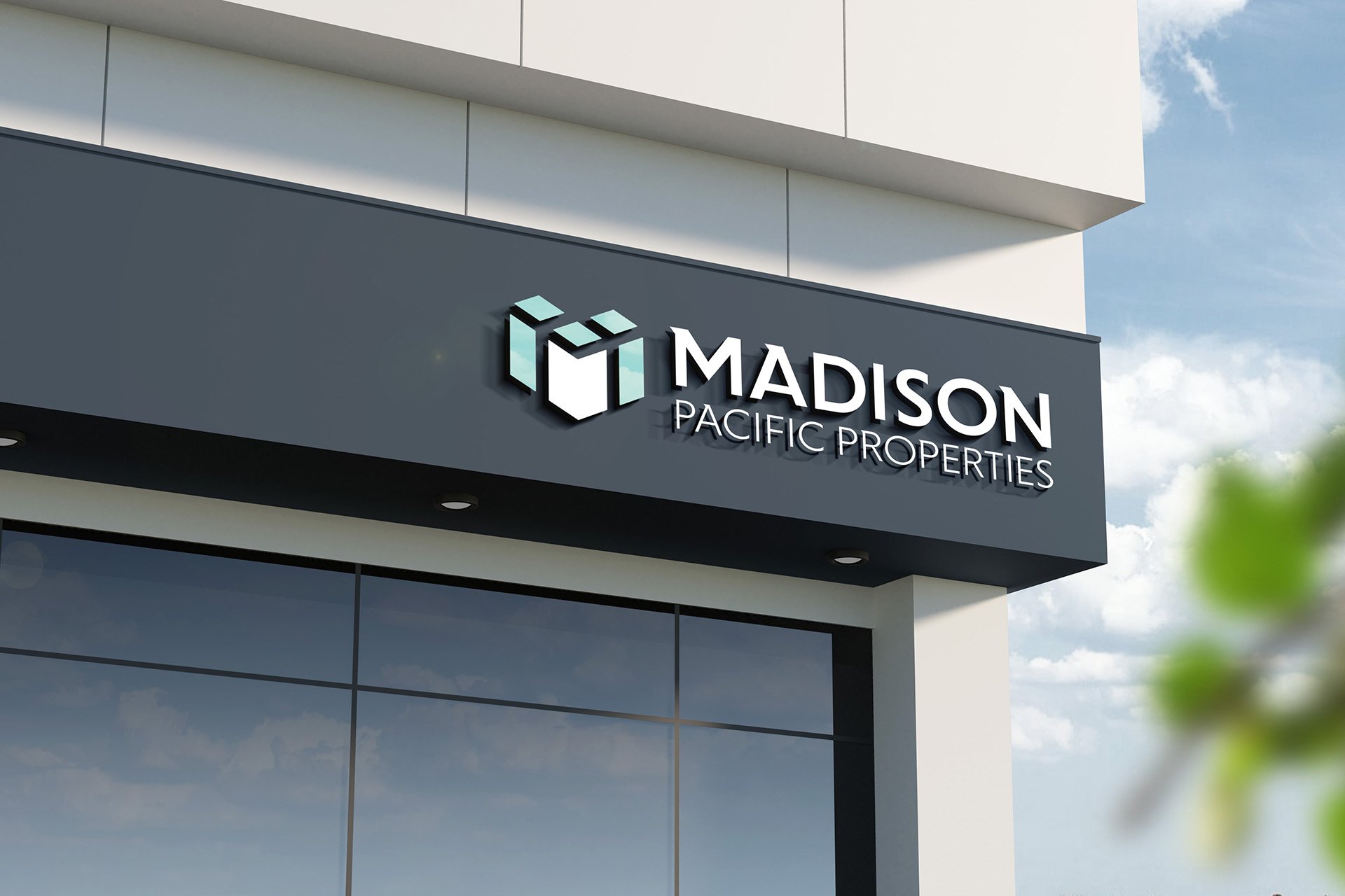 Sign for Madison Pacific Properties on the exterior of a modern building with large reflective windows and a blue sky with clouds in the background.