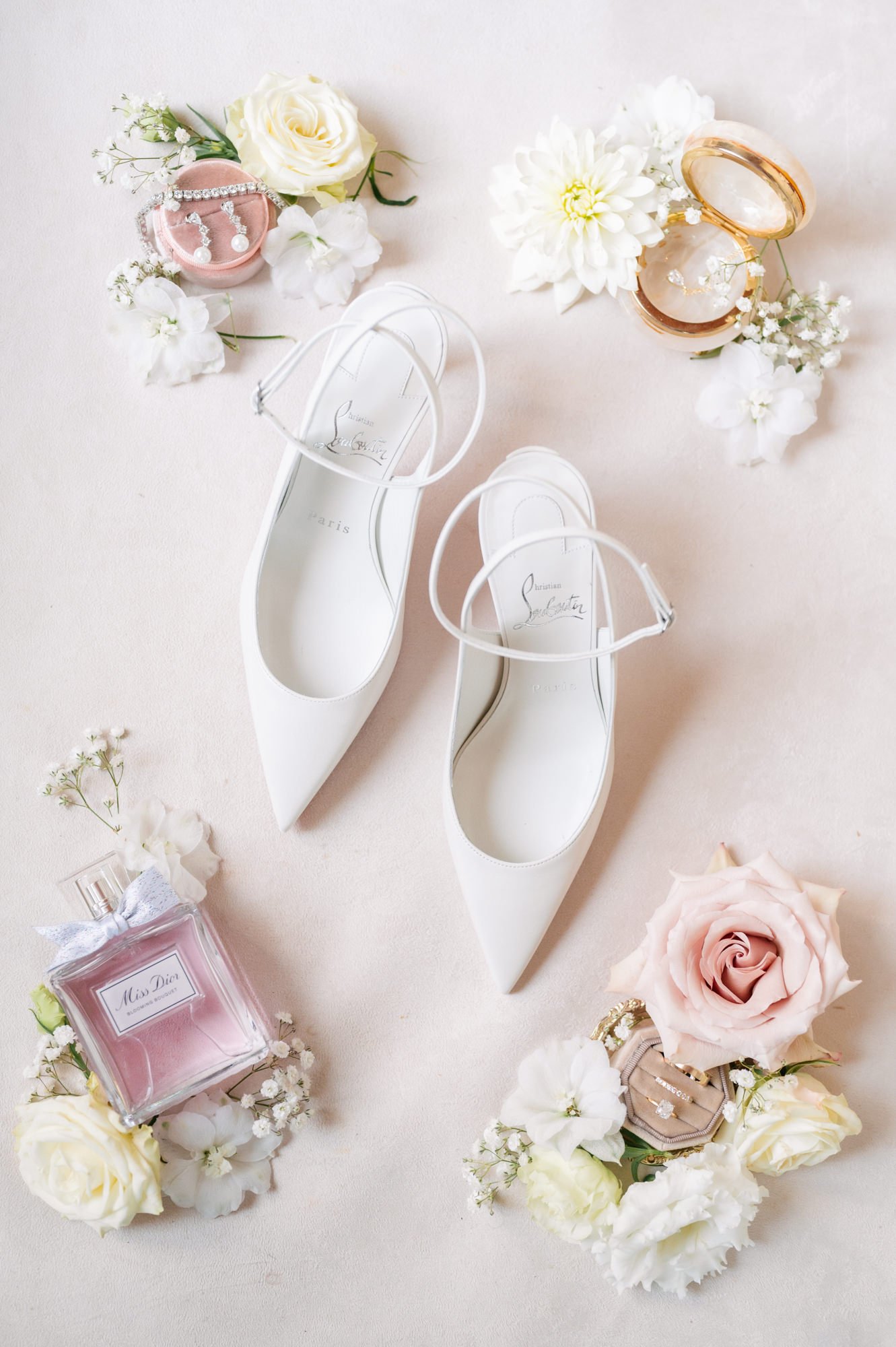White high-heeled shoes surrounded by flowers, jewelry, and perfume bottles