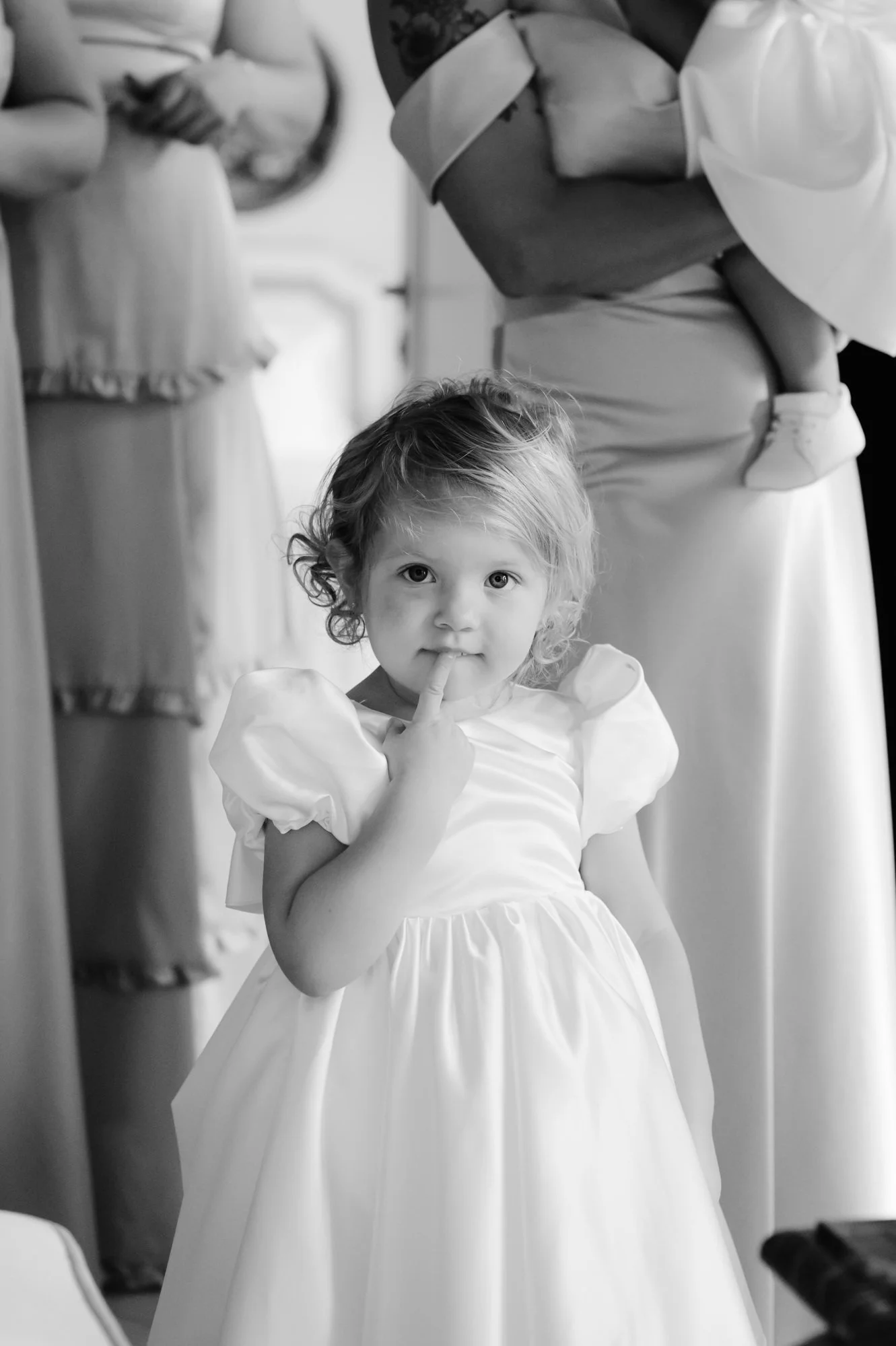 A young girl in a white dress with puffed sleeves, looking directly at the camera with her finger on her lips. Luxury editorial wedding photography in Tuscany. Destination wedding in Italy. L&V Photography Letizia Maccarini.