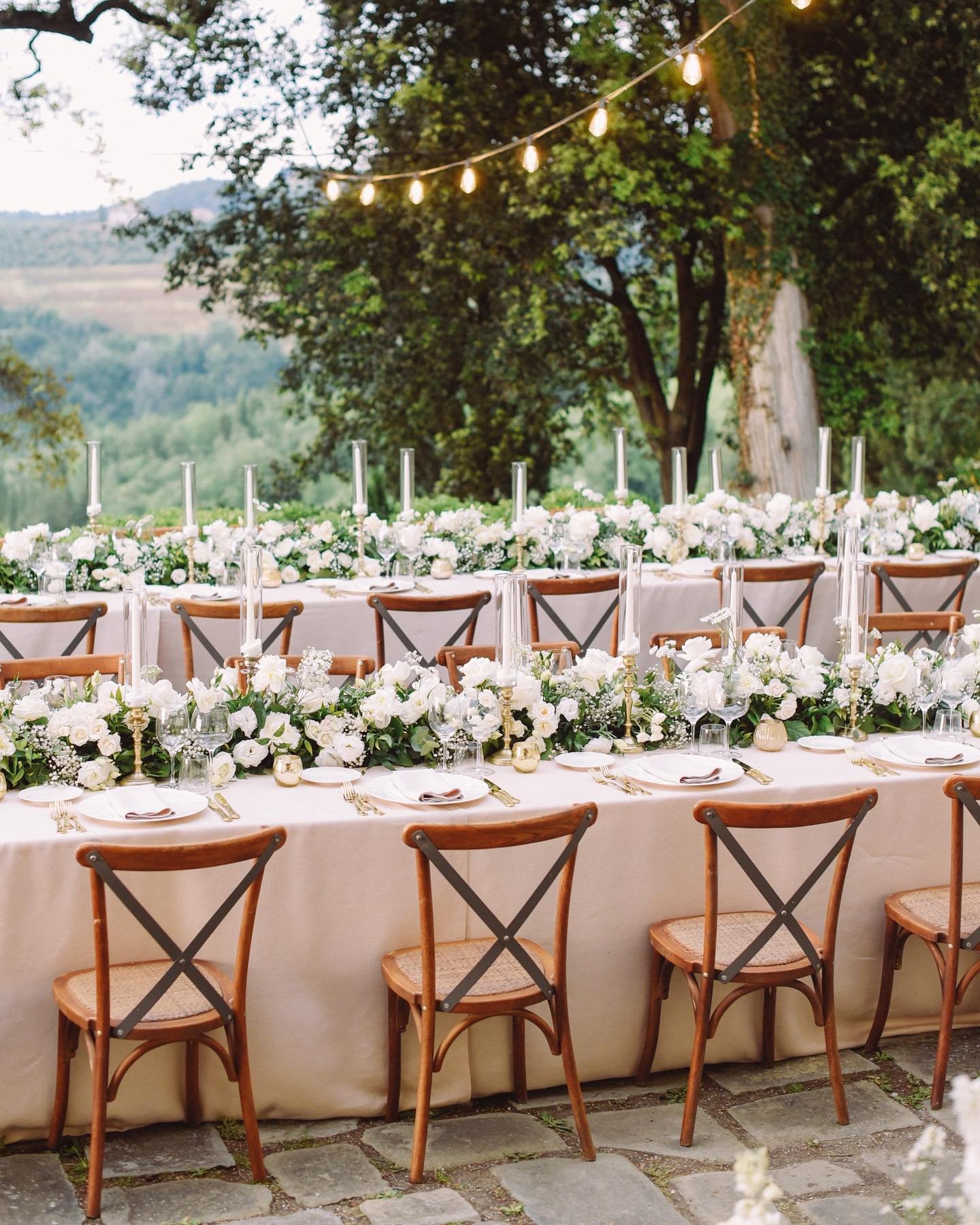 Step into this unique reception: two long imperial tables adorned with delicate white floral arrangements, golden candlesticks and precious tea lights under fairy lights. A true Tuscan dream! 

Wp: @paolocicognani_weddingsitaly 
Venue: @tenutasticcia