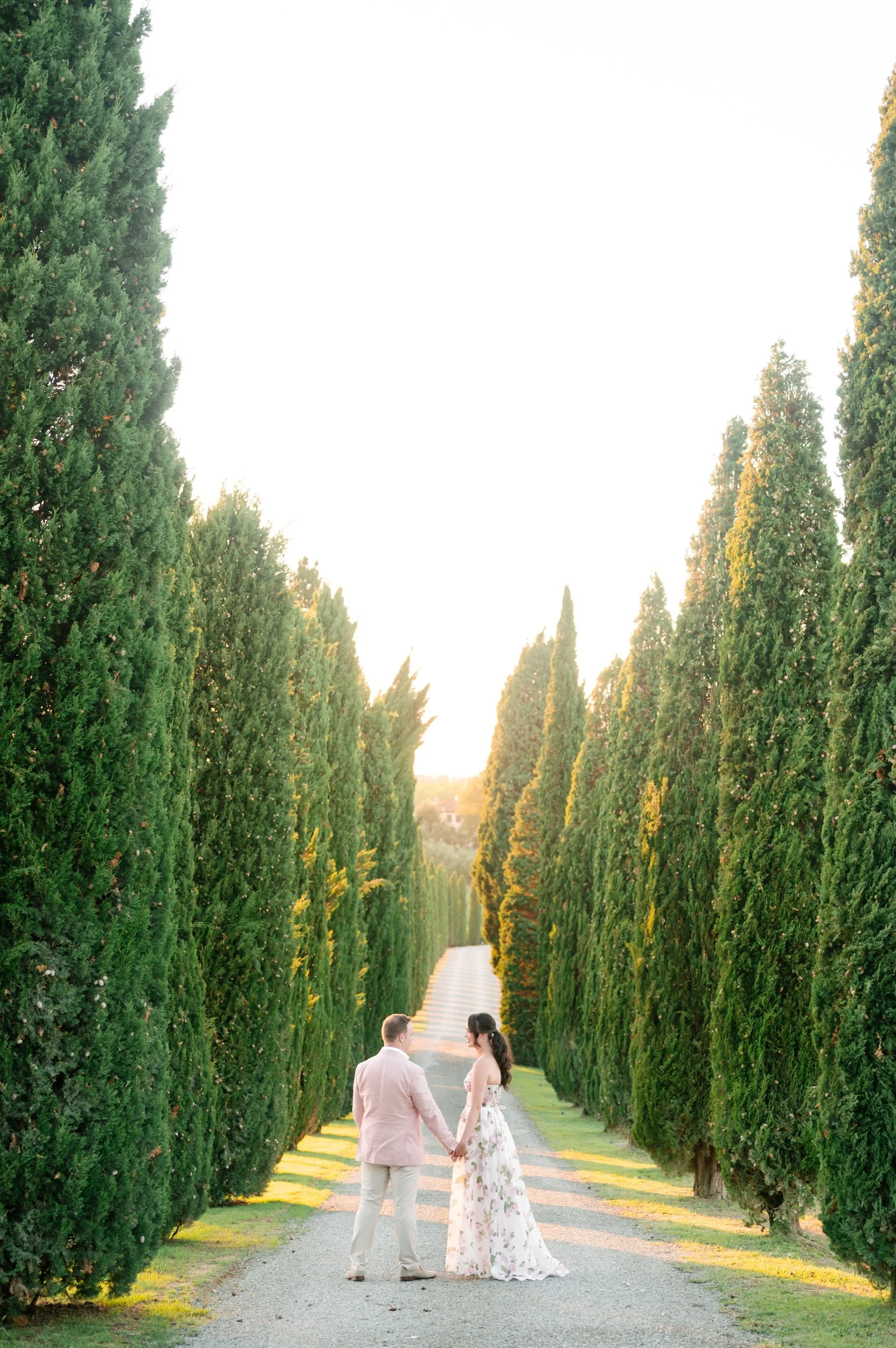 Couple holding hands walking down a tree-lined path during sunset.