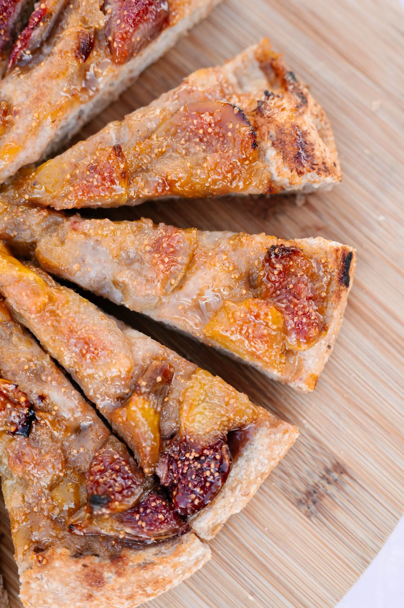 Slices of homemade fruit and nut tart with a sweet glaze on a wooden cutting board.
