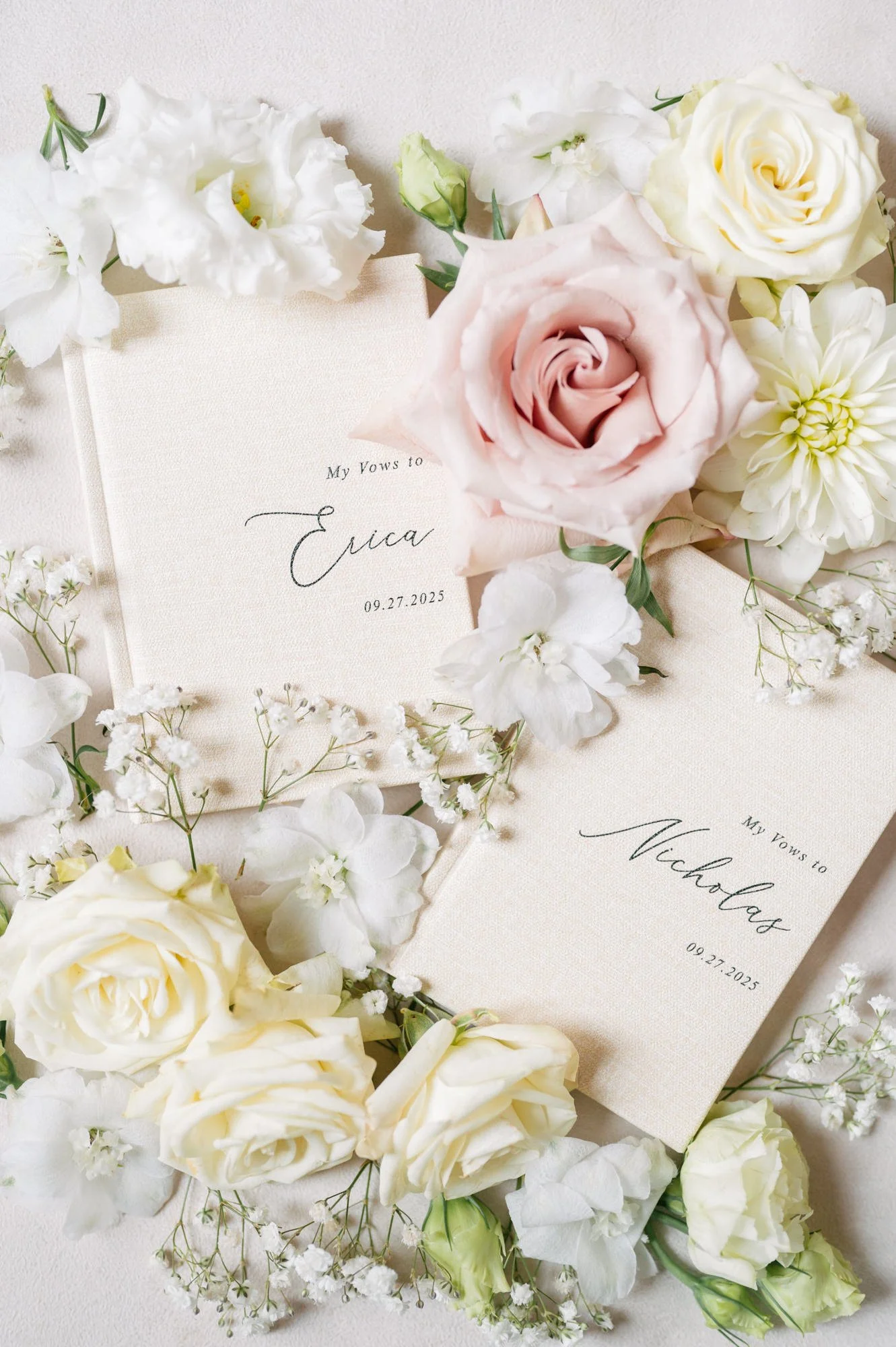 A wedding invitation surrounded by white and blush roses, baby's breath, and other white flowers.