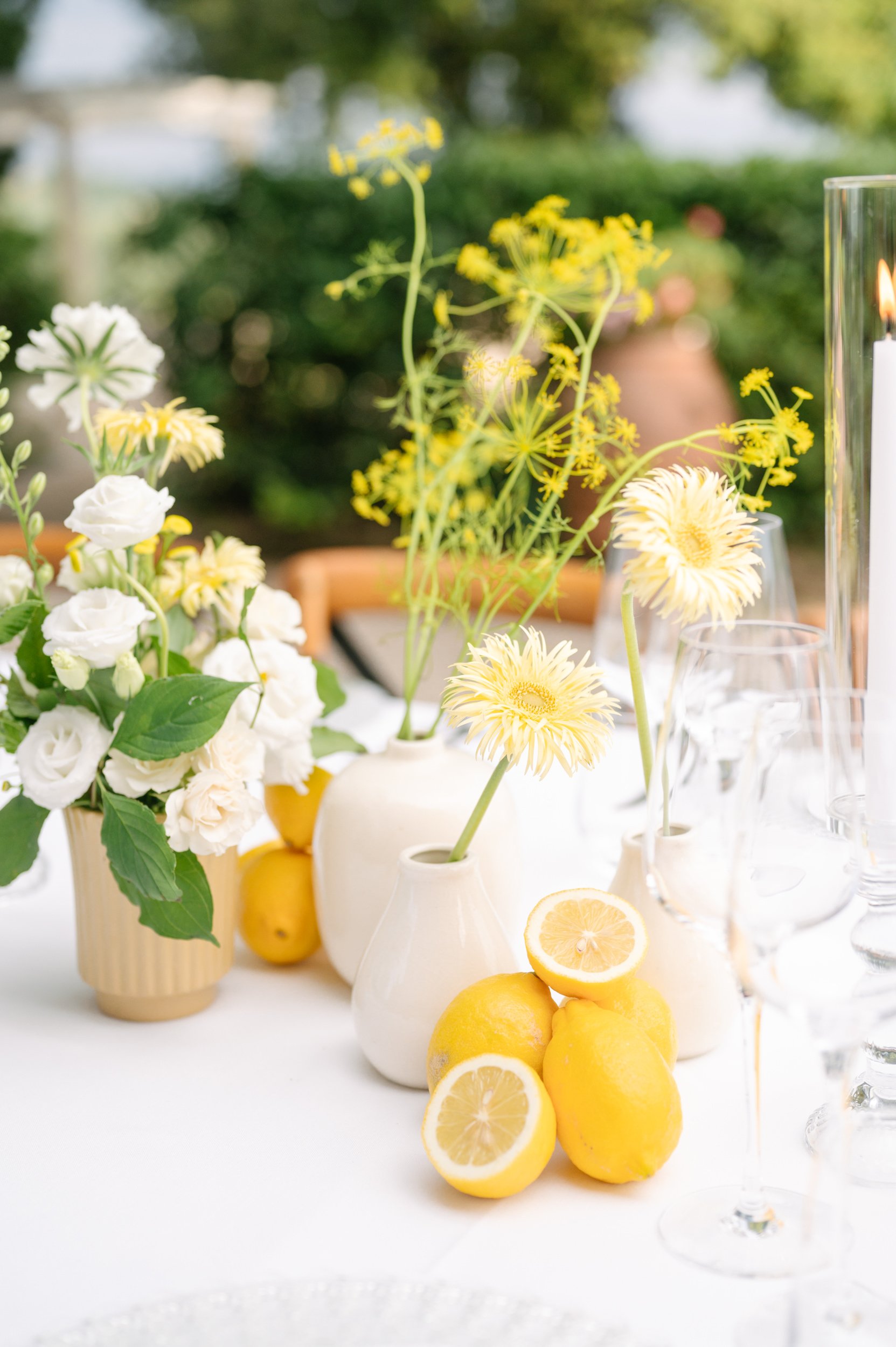 Table decorated with white and yellow flowers, lemons, and glassware in an outdoor setting.