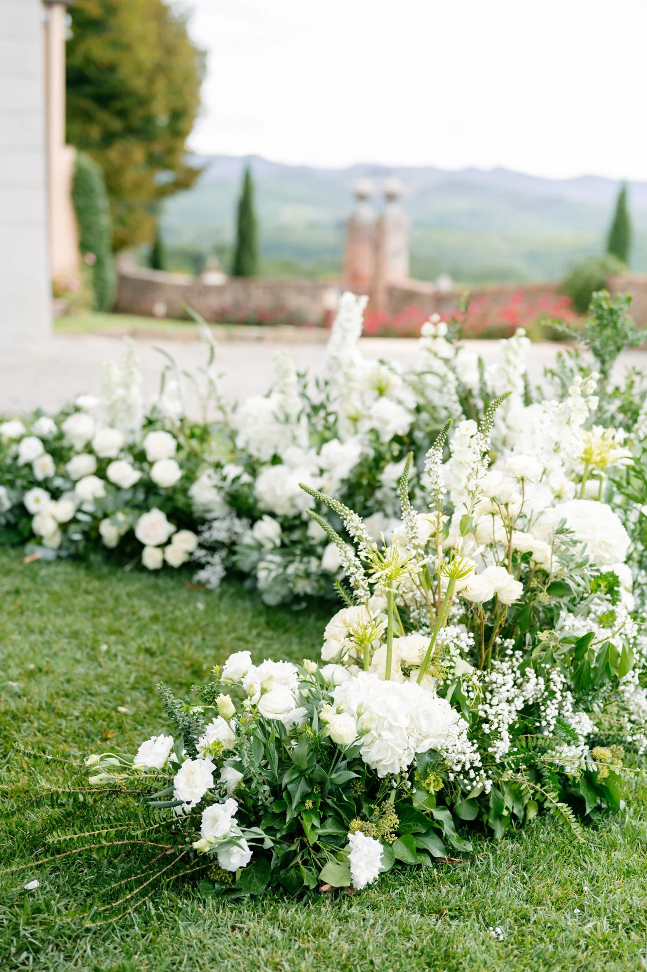 White floral arrangement on green grass at an outdoor wedding or special event, with blurred landscape background. Luxury editorial wedding photography in Tuscany. Destination wedding in Italy. L&V Photography Letizia Maccarini.