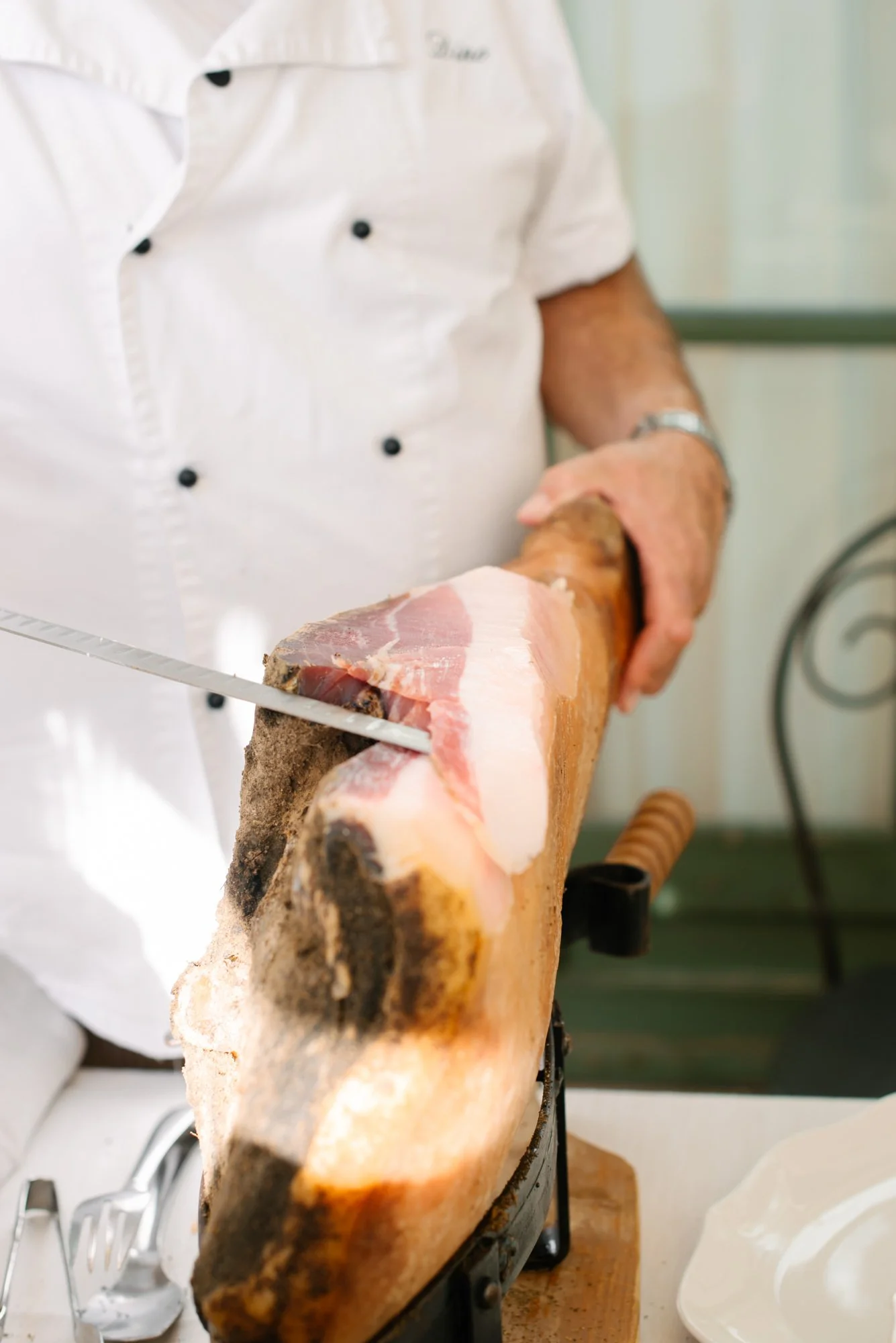 Chef slicing cured ham or prosciutto on a large wooden ham holder.