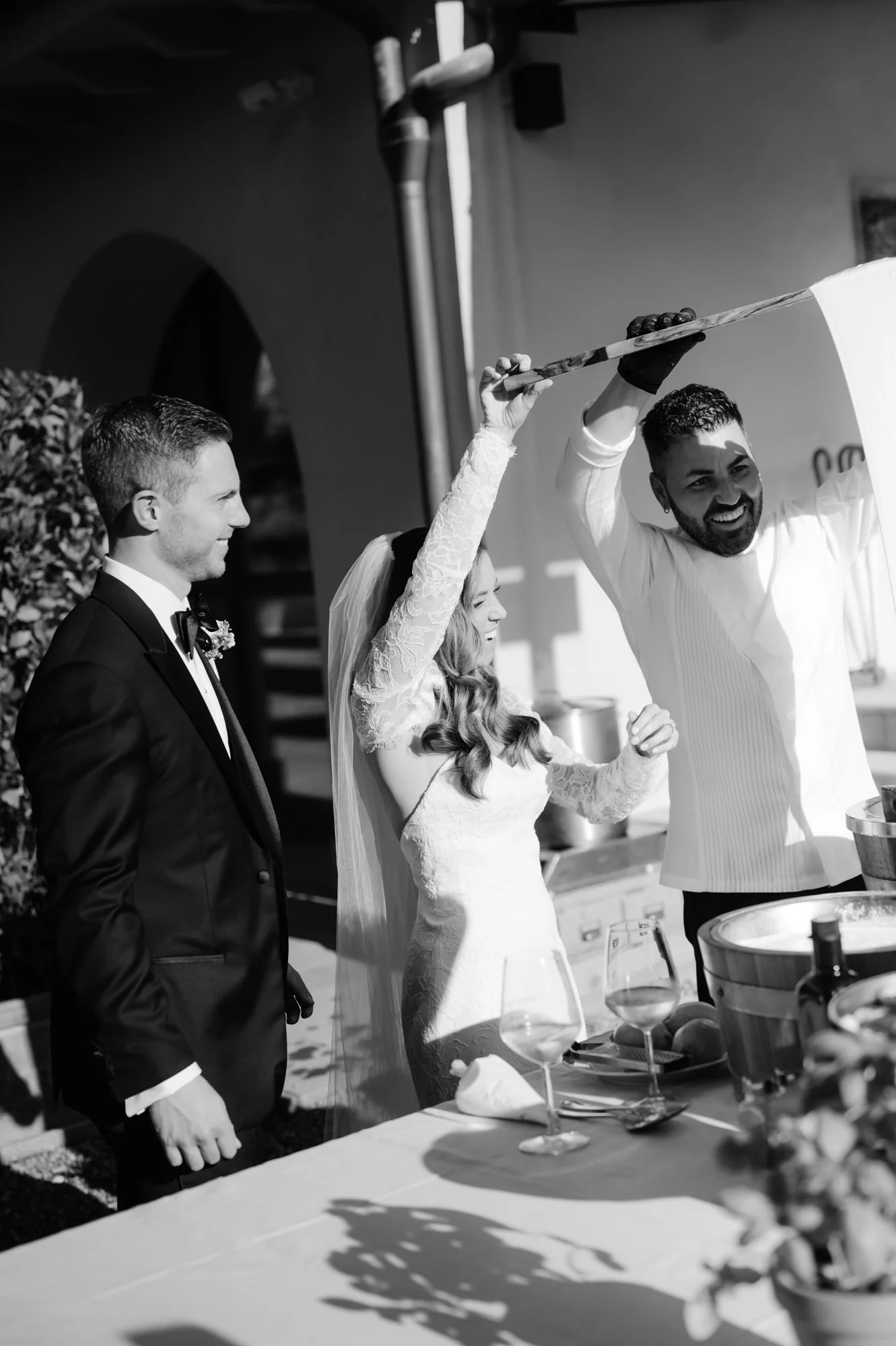 Black and white photo of a wedding ceremony with a groom and bride watching a chef serve food with a long spoon.