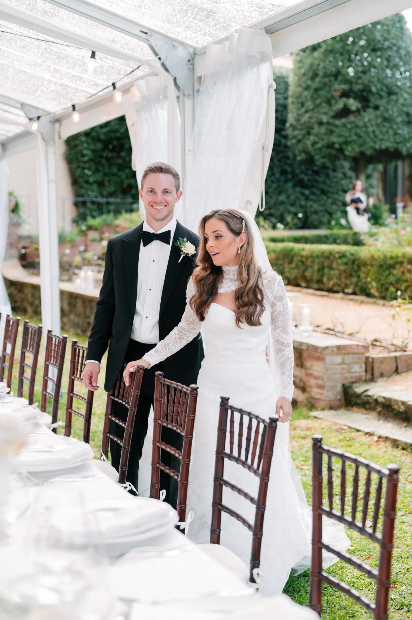 A bride and groom standing together during their wedding reception outdoors under a canopy with string lights, with tables and chairs set up for the celebration.