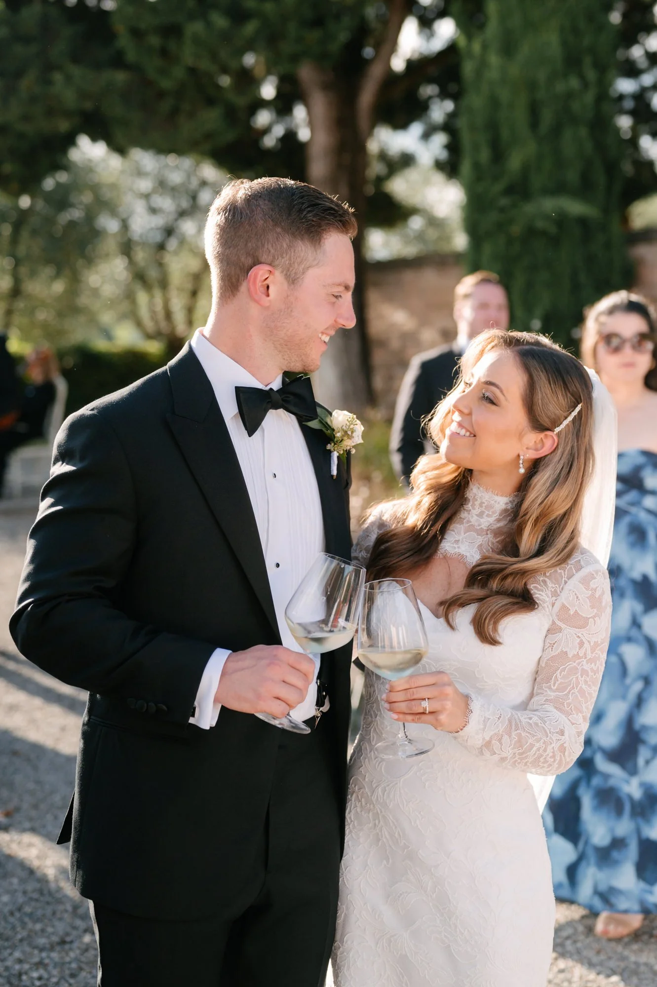 Bride and groom smiling at each other holding wine glasses during a wedding reception outdoors. Luxury editorial wedding photography in Tuscany. Destination wedding in Italy. L&V Photography Letizia Maccarini.
