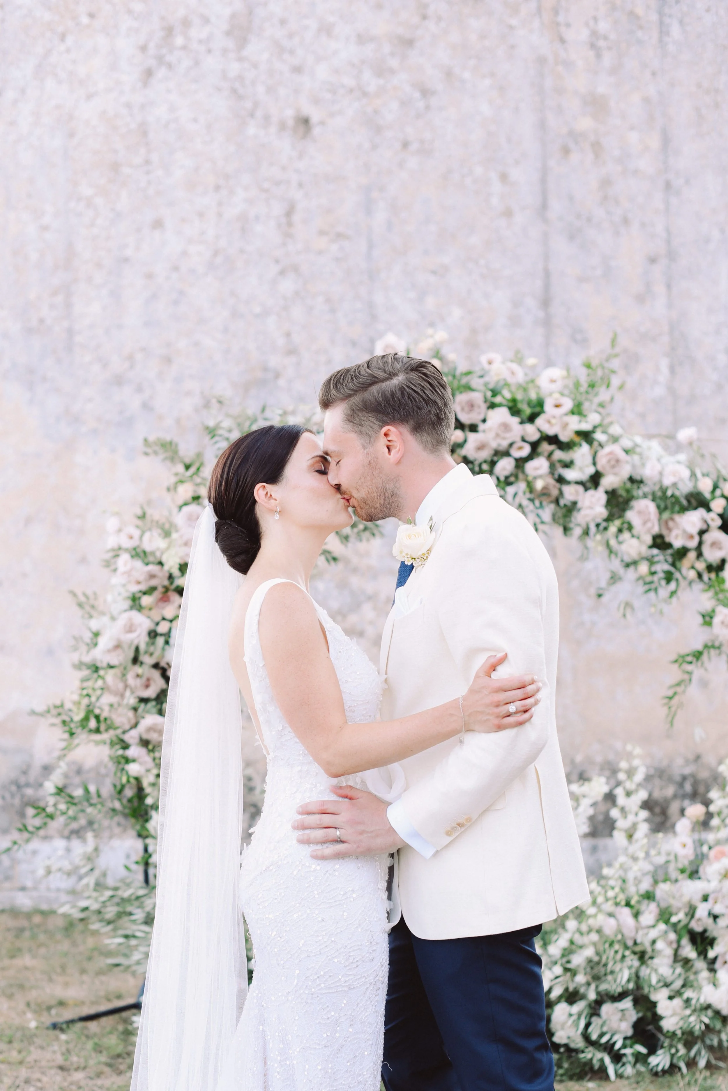 Wedding couple kissing in front of floral arch on outdoor ceremony