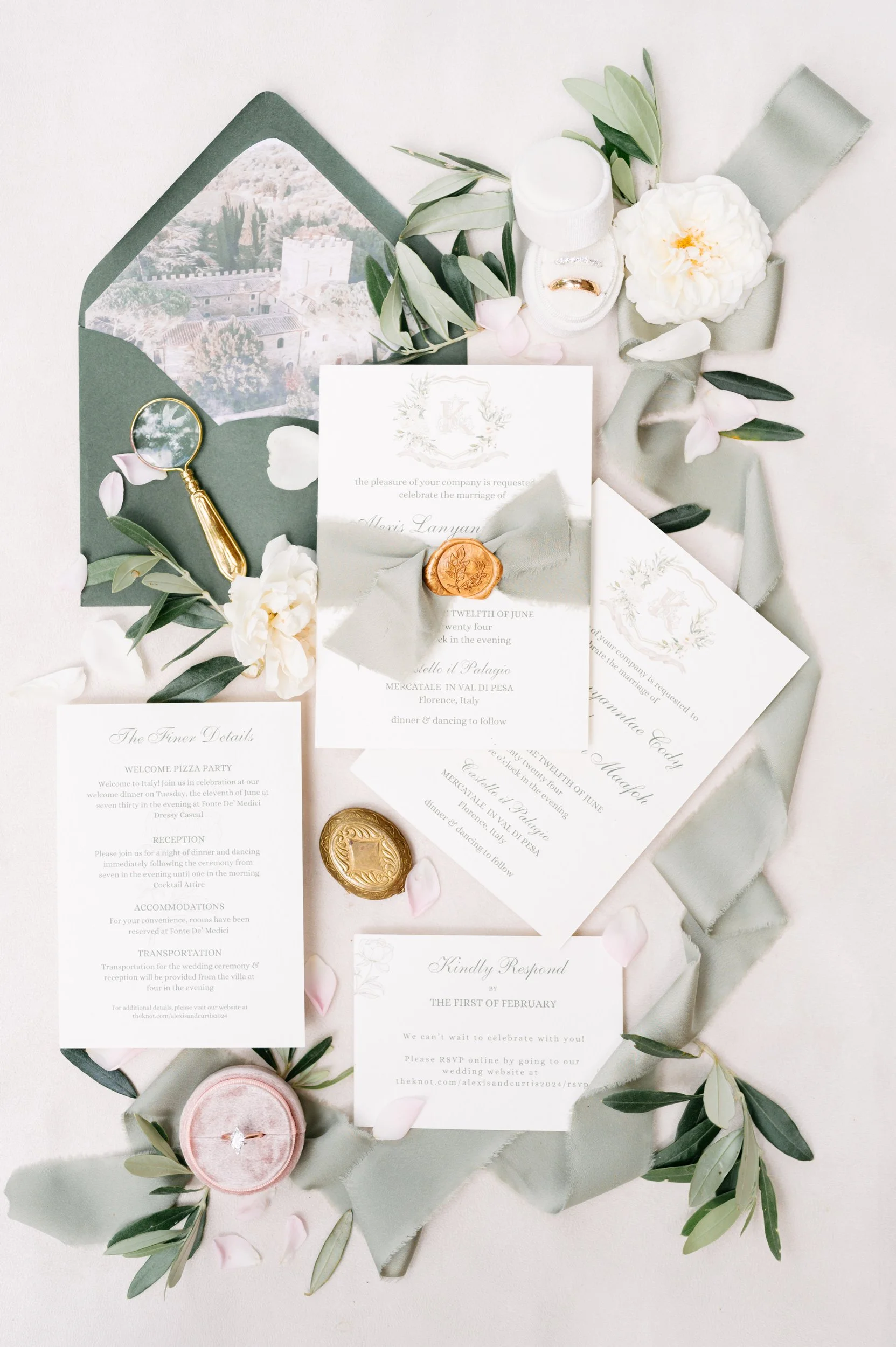 Wedding invitation suite with greenery, flowers, vintage rings, and gold wax seal, arranged with an envelope, candles, and a small magnifying glass.
