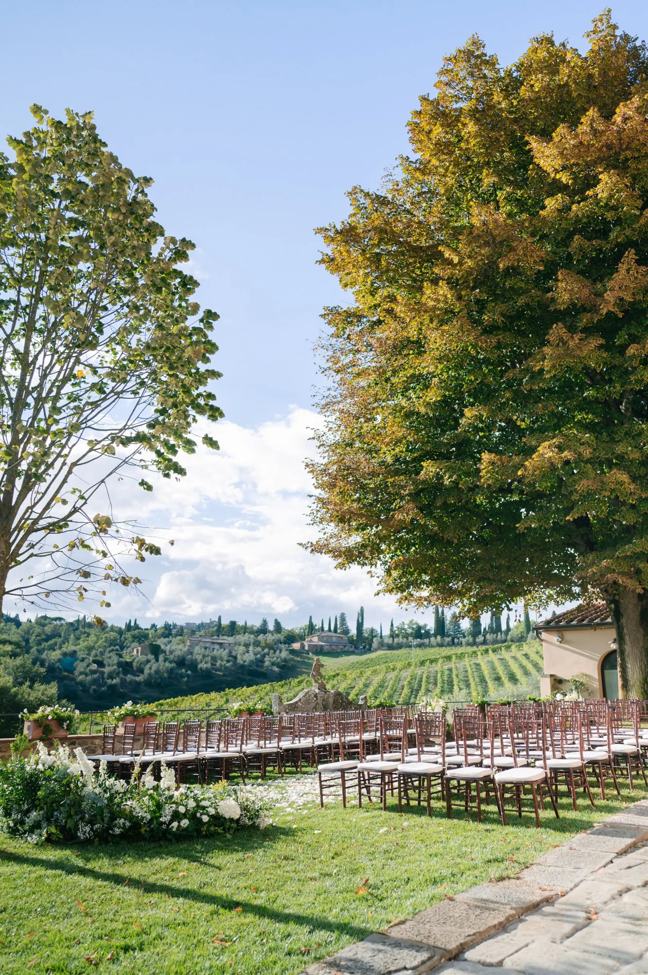 Outdoor wedding ceremony setup with rows of chairs, floral arrangements, and scenic vineyard landscape in the background.
