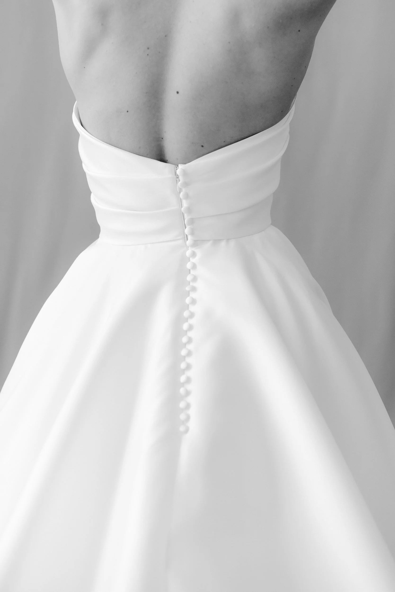 Close-up of a backless wedding dress with a row of buttons down the back and a full skirt.
