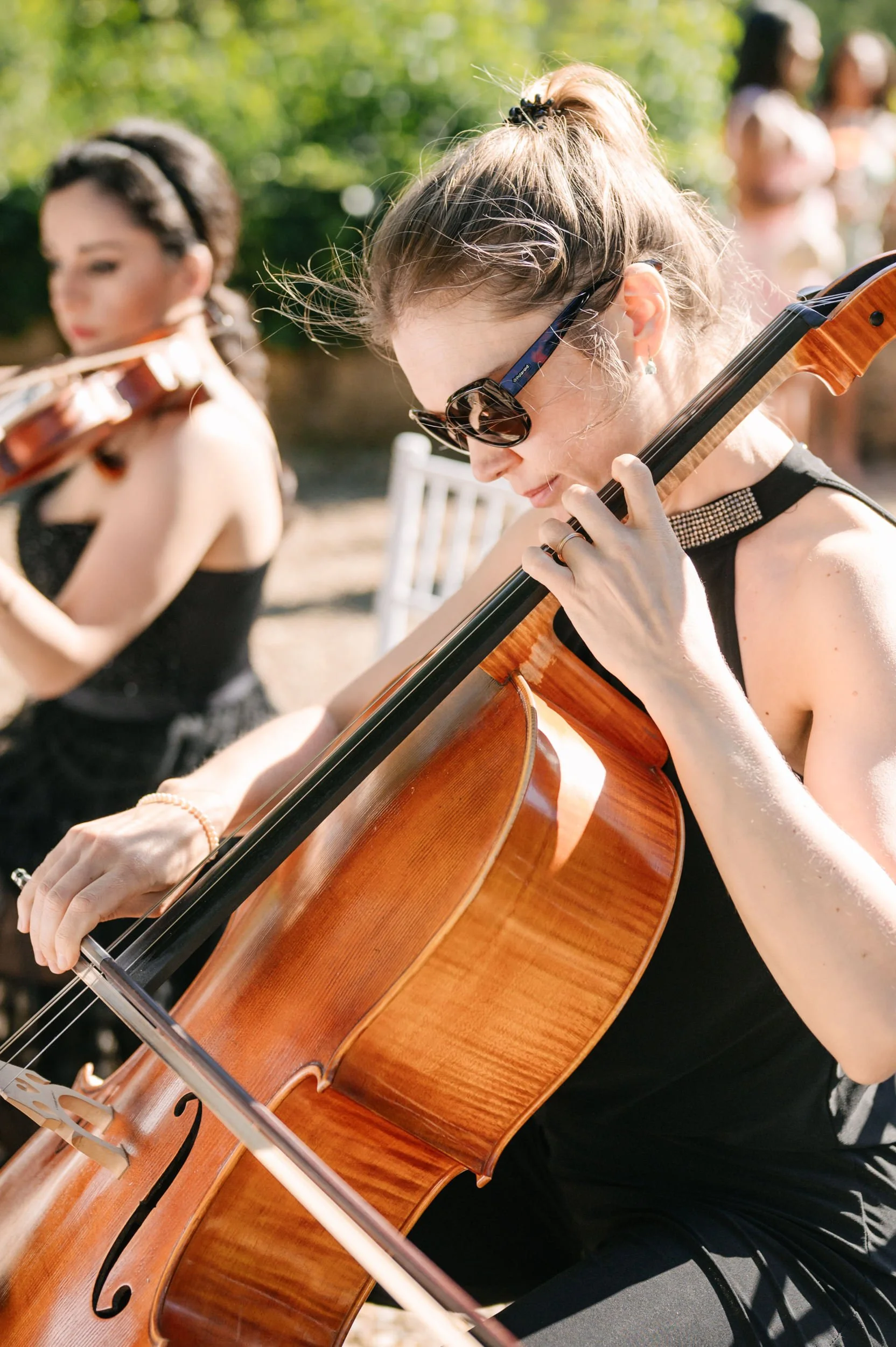 Women playing violins outdoors at a sunny event.