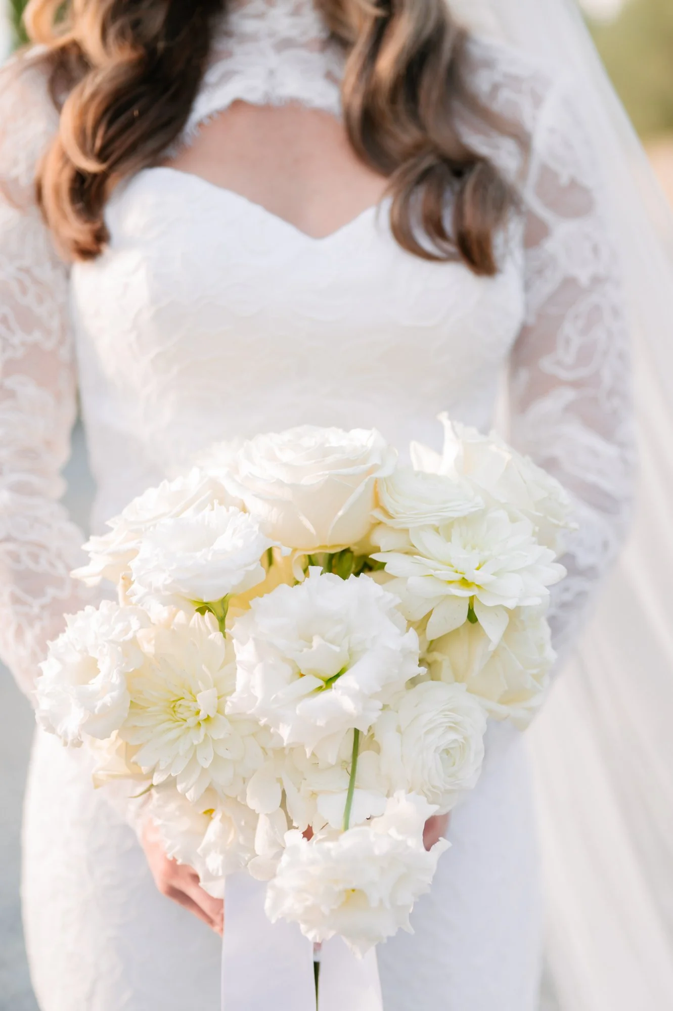 A bride in a lace wedding dress holding a bouquet of white flowers.