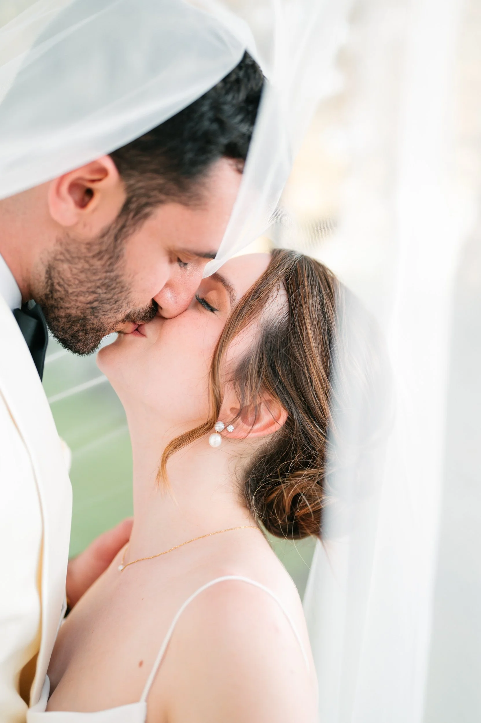 A bride and groom sharing a kiss under a white veil on their wedding day.