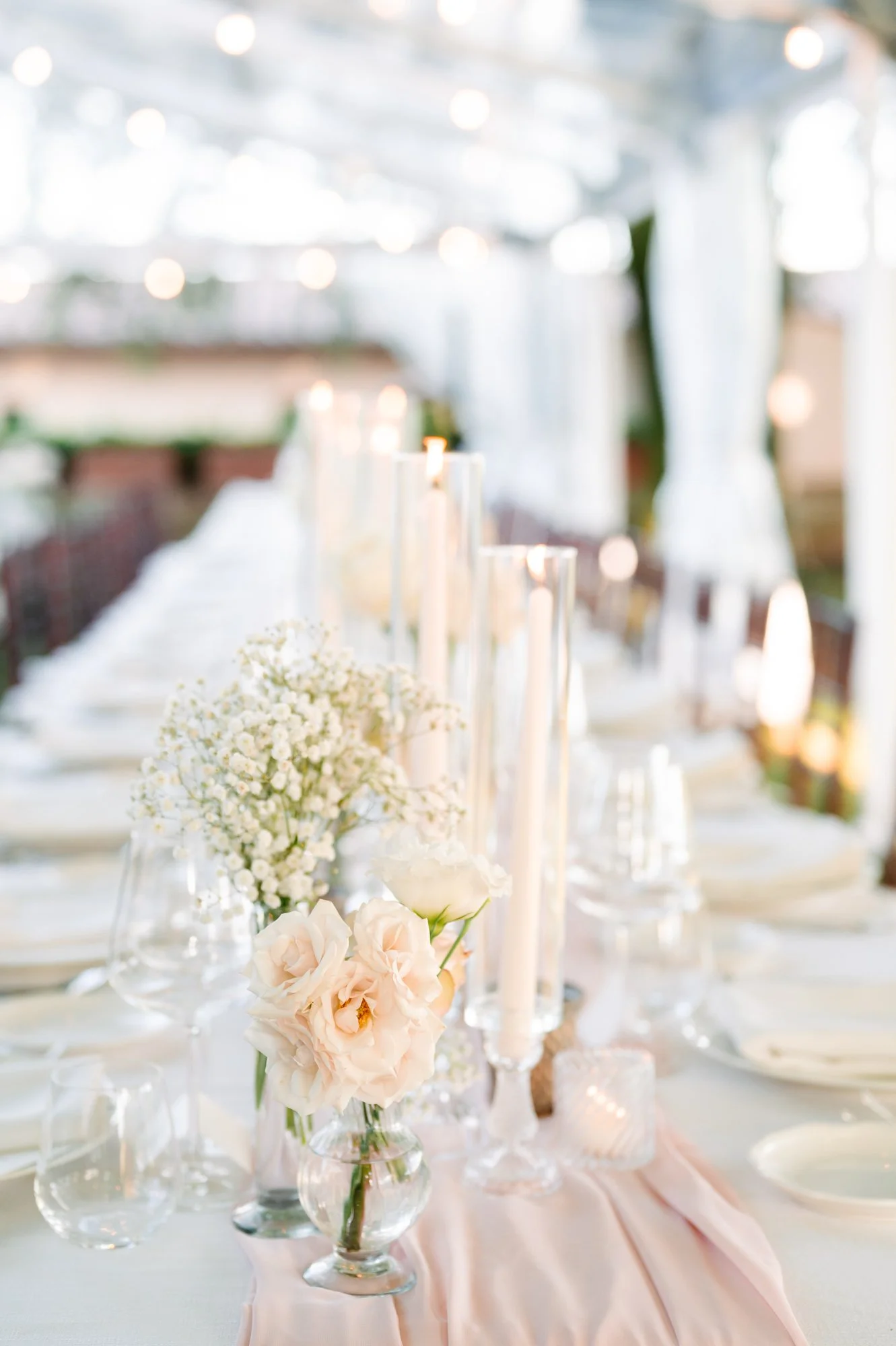 Elegant dining table decorated with pink and white flowers, tall candles, and glassware at a wedding or special event.