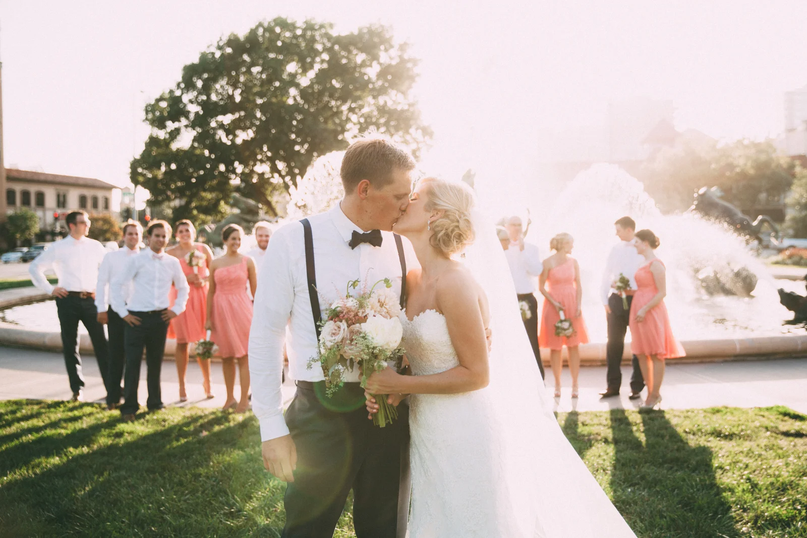 Bride and groom kissing with wedding party in front of famous JC Nichols Kansas City fountain