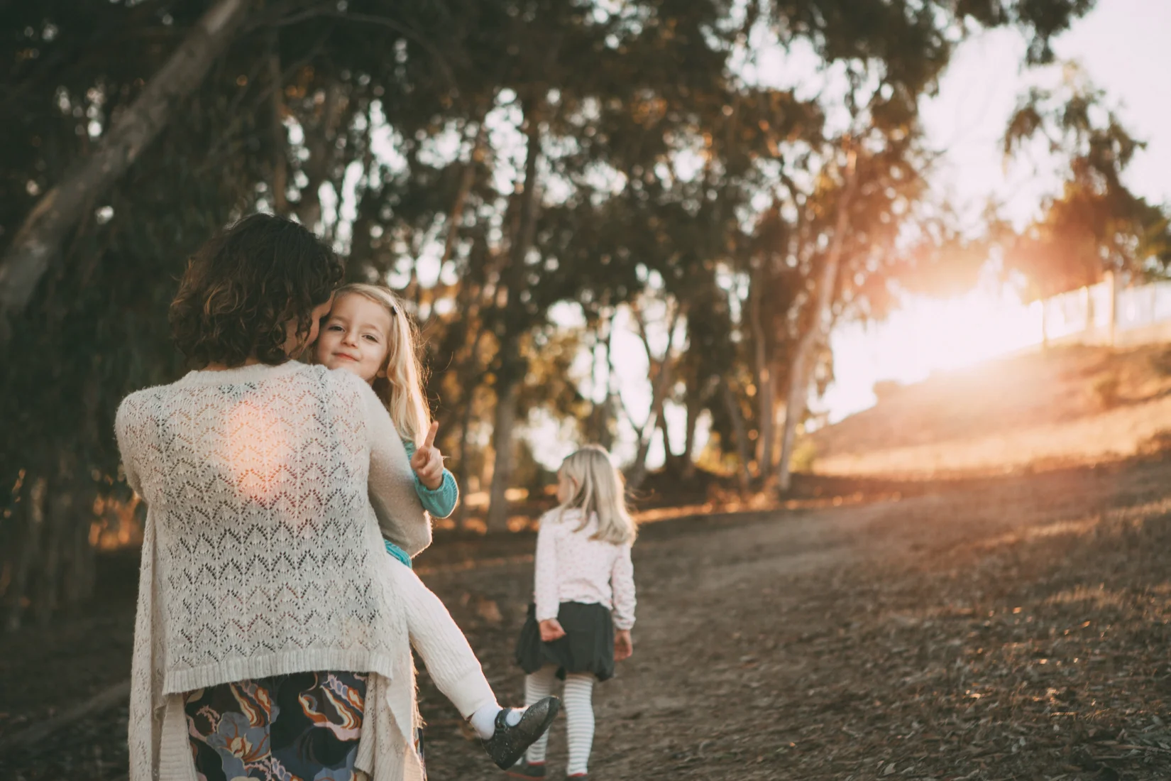Mom holds daughter and walks up hill in the woods at sunset