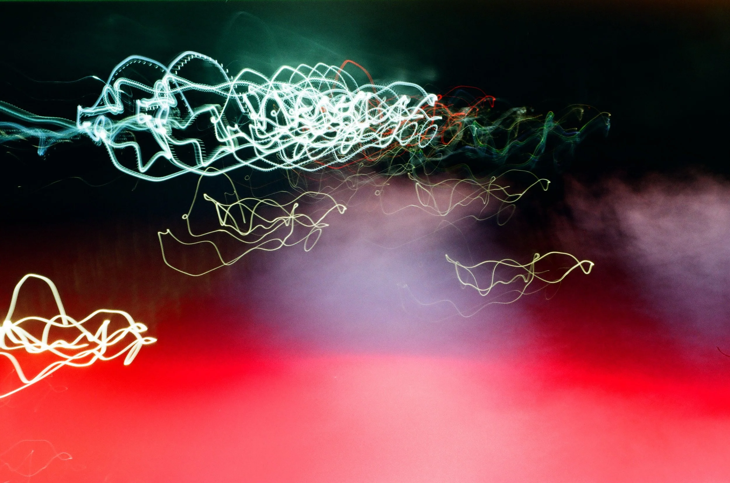 Light trails create abstract patterns over a dark background with red at the bottom.