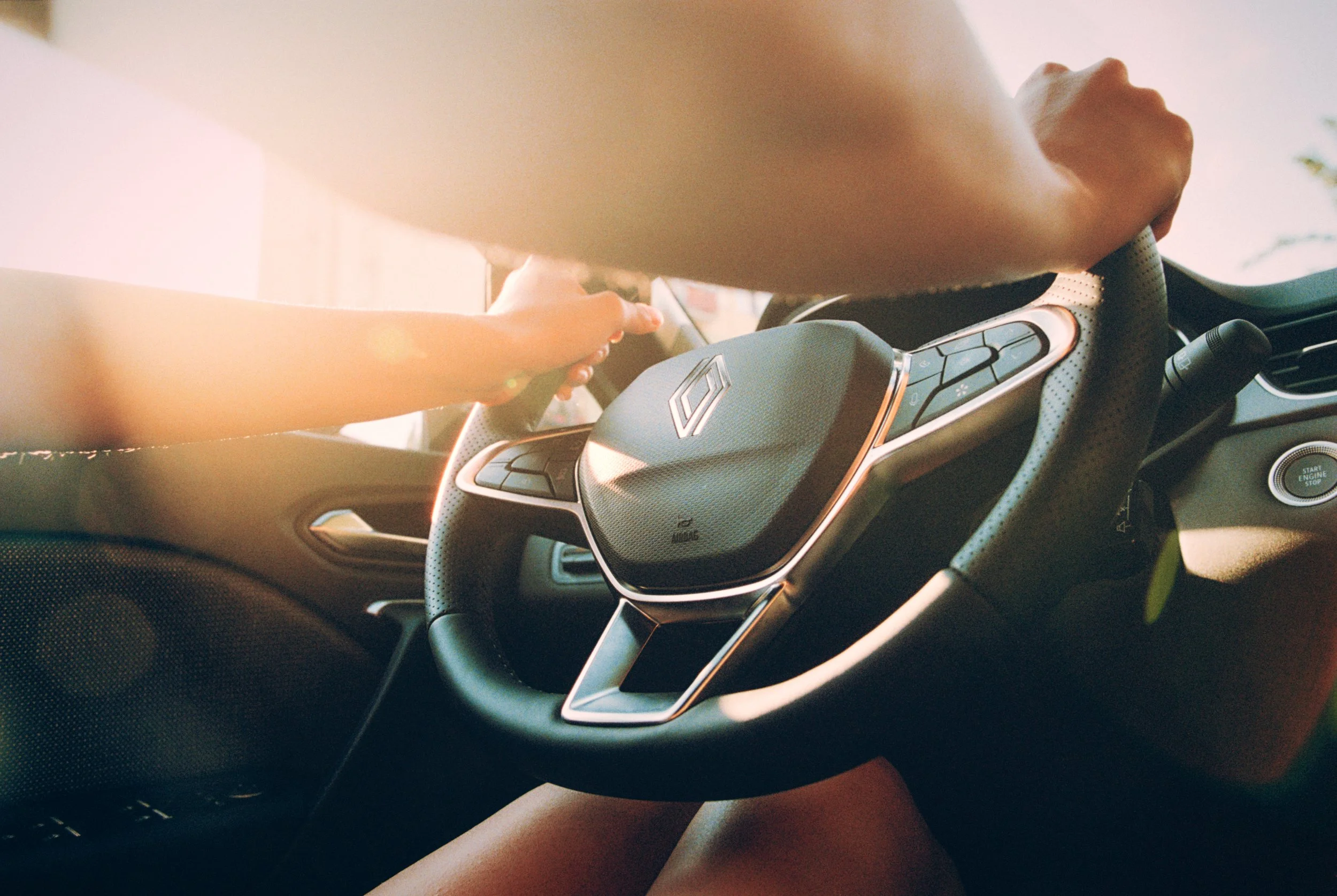 Close-up of a person's hand on a steering wheel inside a modern car, with sunlight shining through the window.