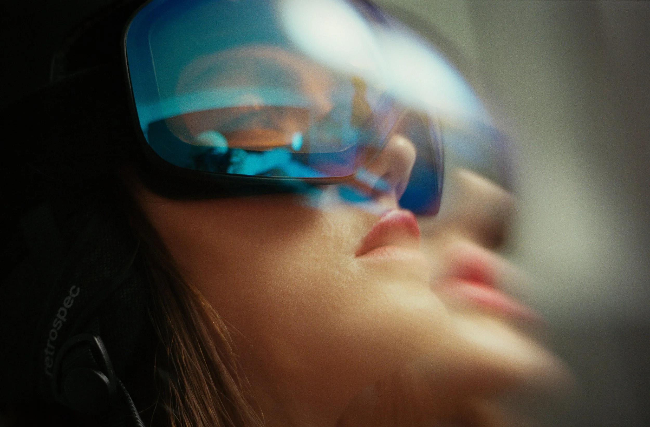 Close-up of a person wearing sunglasses with reflective blue lenses, showing their nose and lips, and part of their face and dark hair.