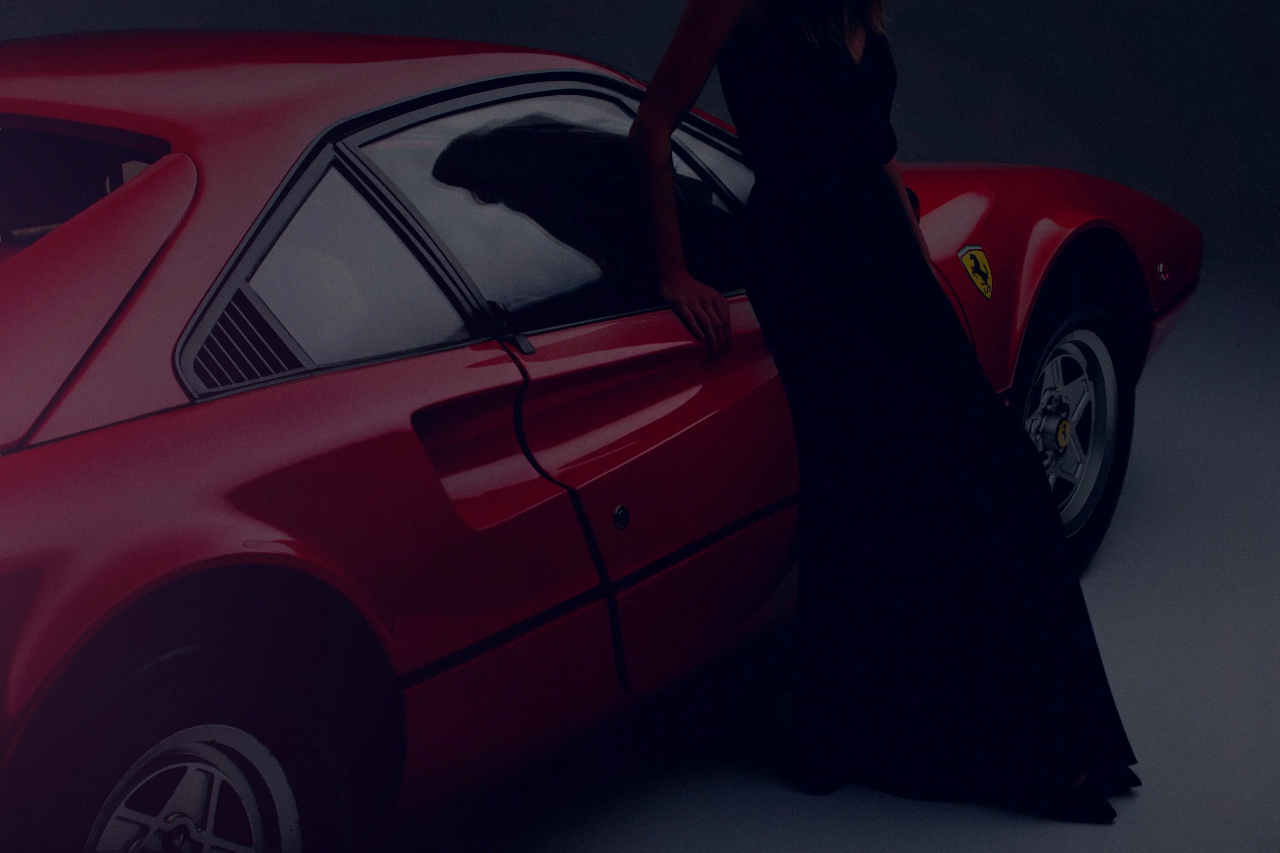 A woman in a black dress leaning on a red Ferrari sports car with the Ferrari logo visible on the front. The scene is dark with a focused light highlighting the car's curves.