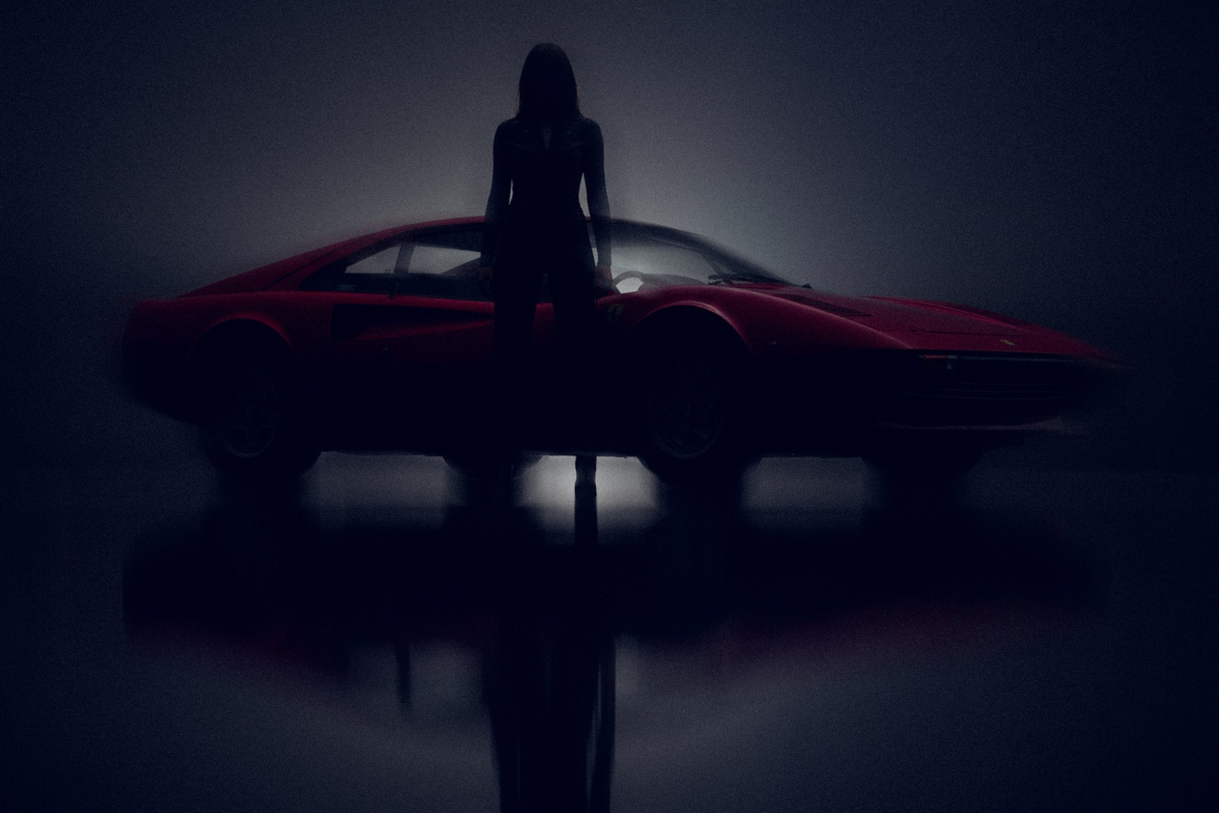 Silhouette of a woman standing behind a red sports car in a dark, minimalistic setting with a reflection on the floor.