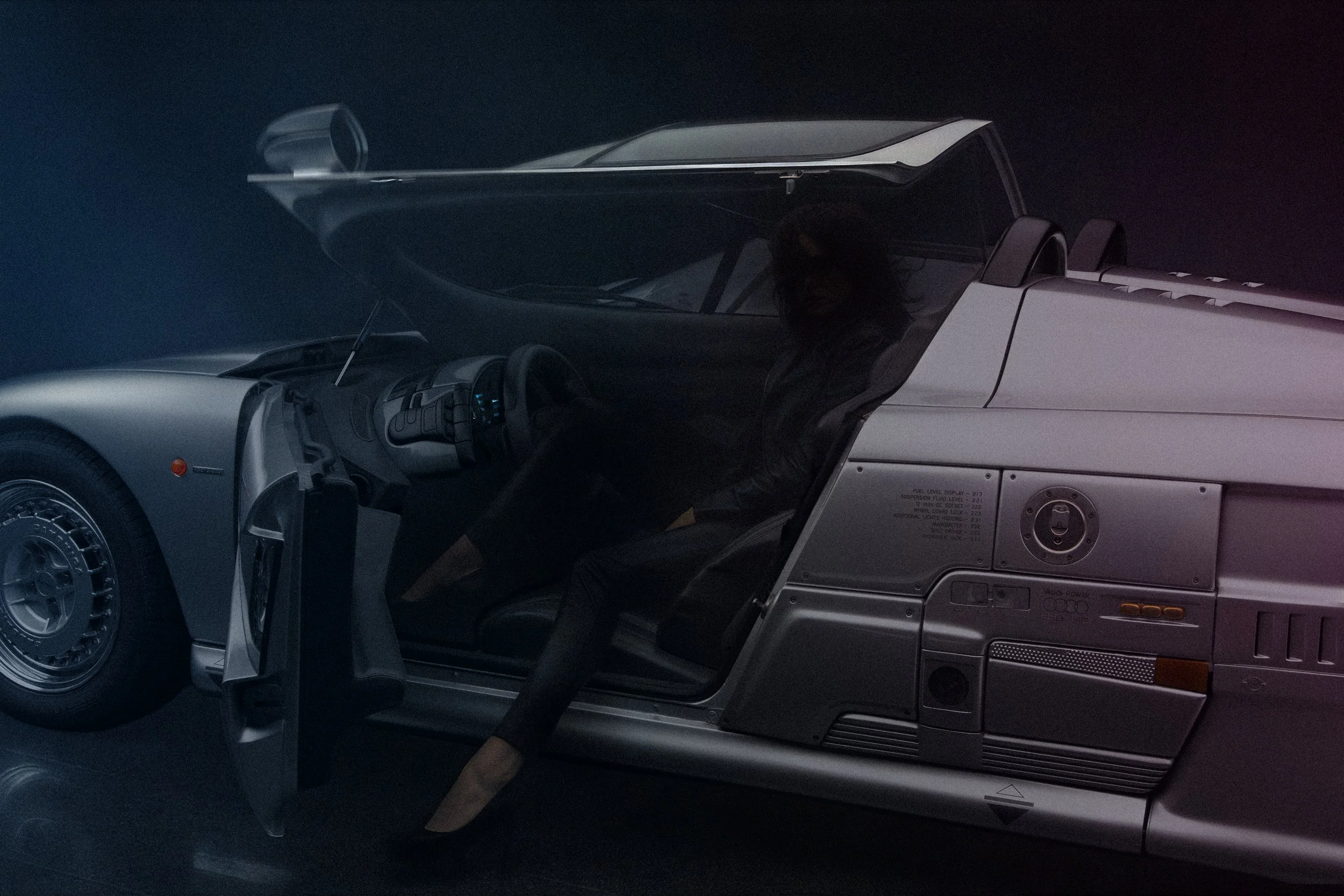 A woman sitting inside a silver, futuristic vehicle with a transparent canopy, in a dark environment.