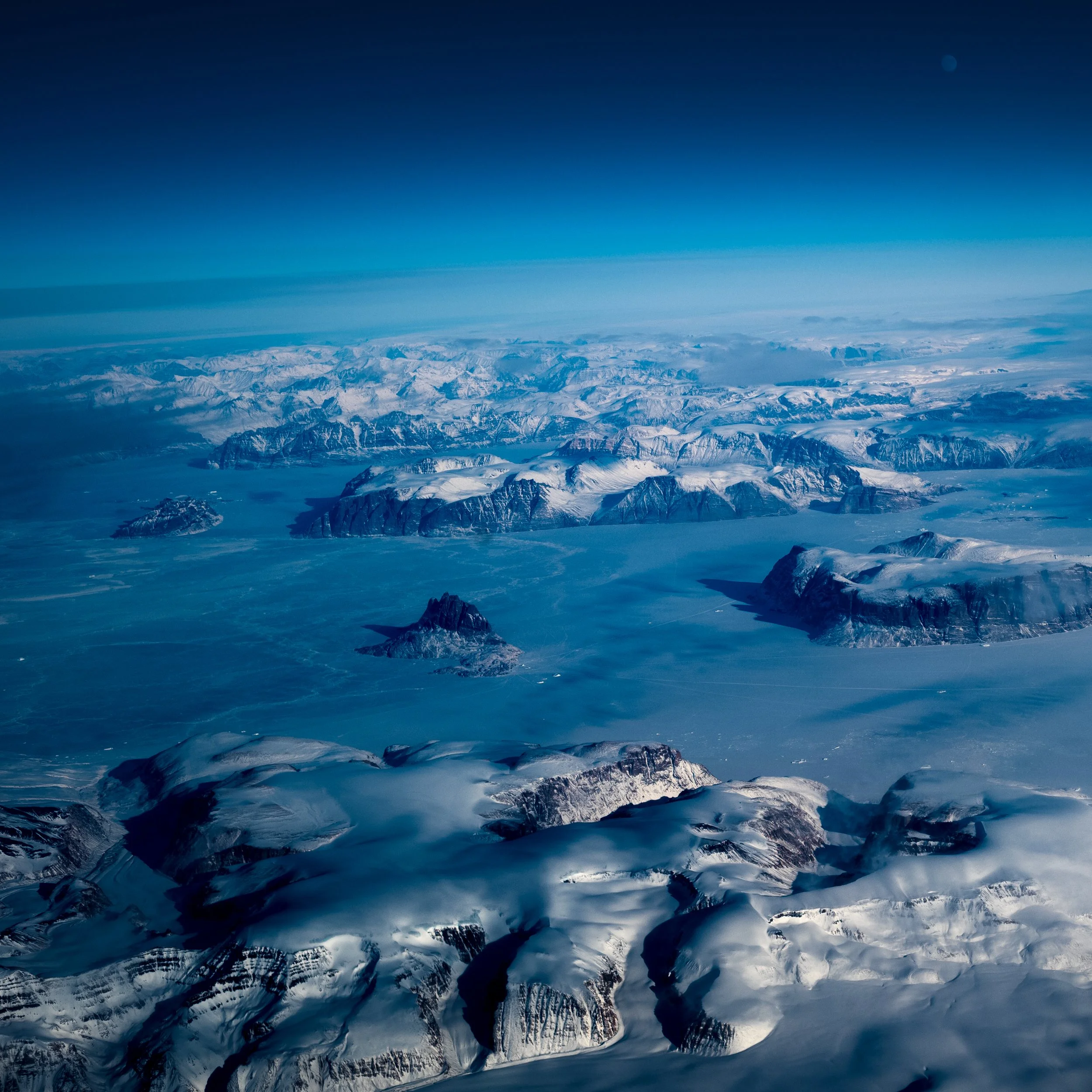 Aerial view of snow-capped mountains and icy terrain under a blue sky.