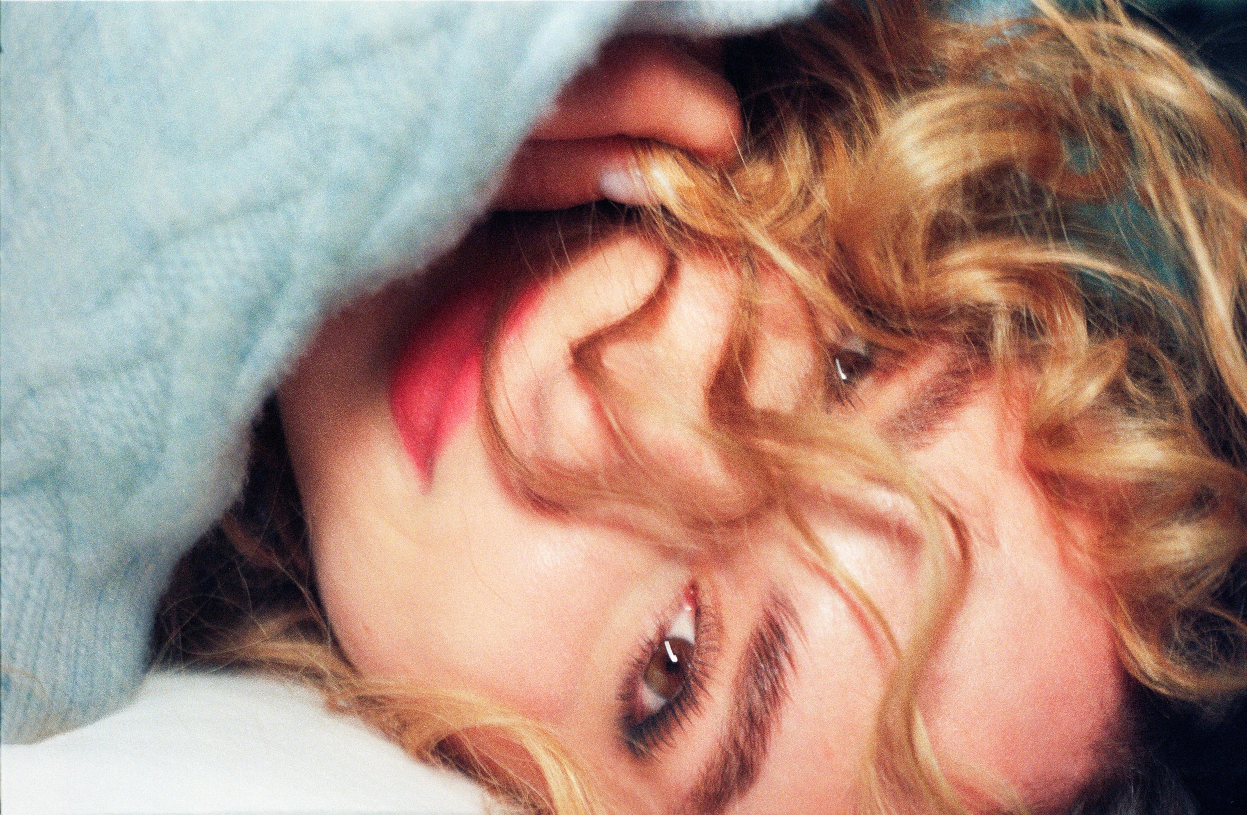 Close-up of a woman with curly blonde hair lying down, looking at the camera.