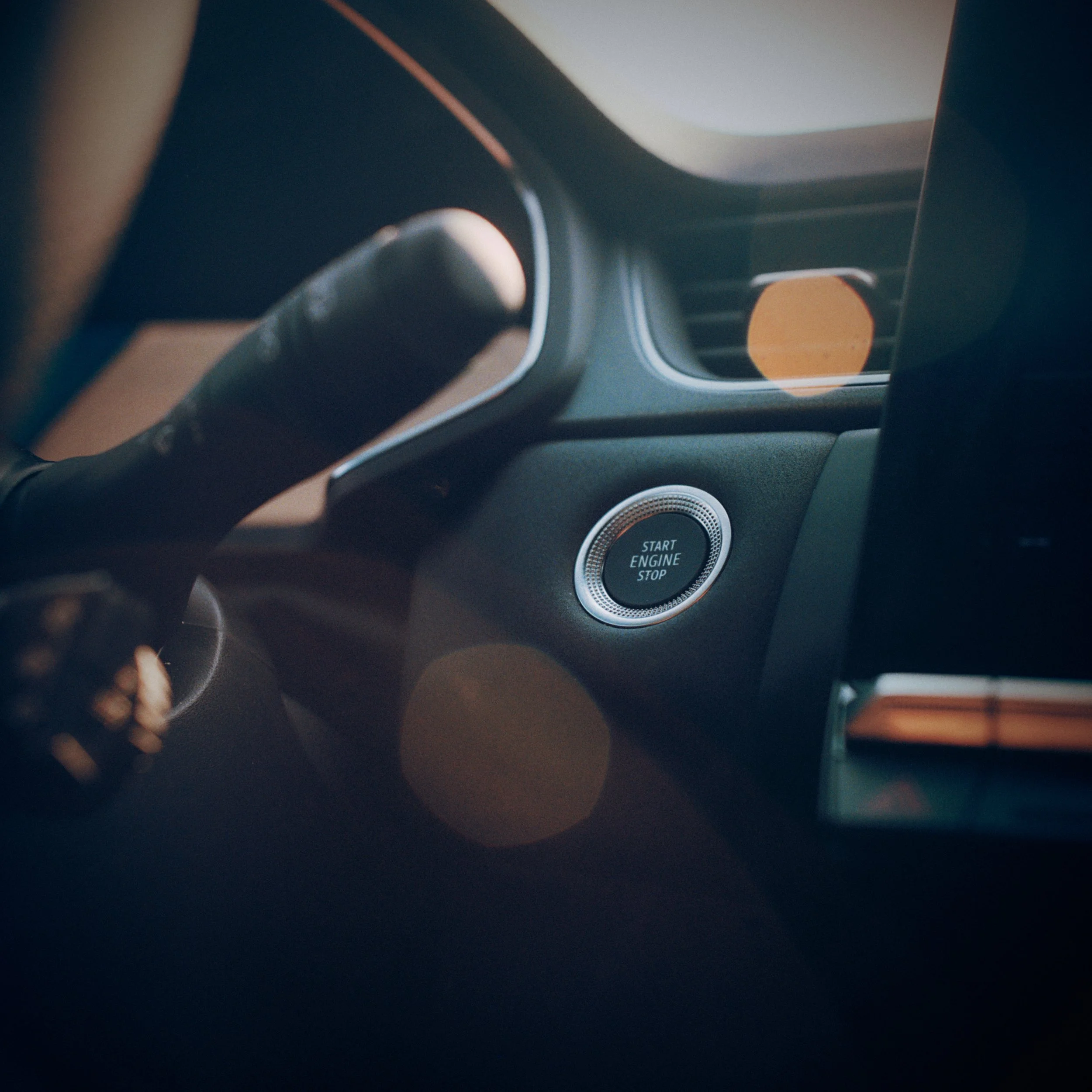Close-up of a car dashboard and start engine button with surrounding dashboard features.