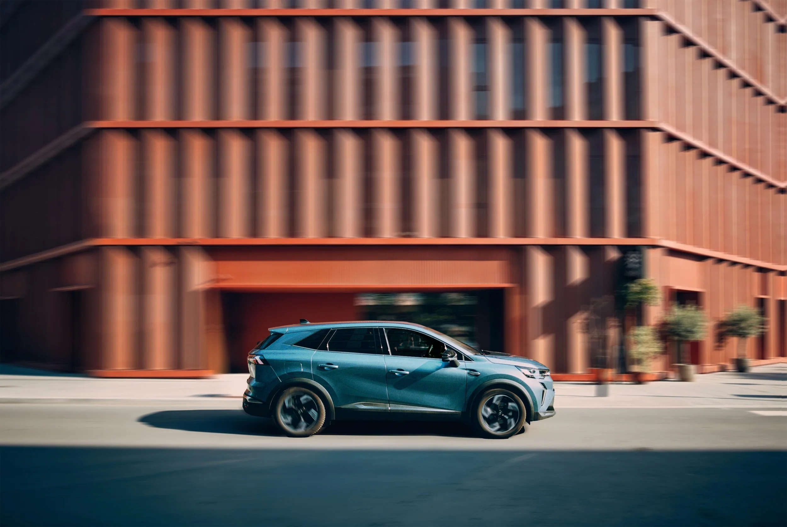 A blue SUV driving past an orange building with vertical white window panels.