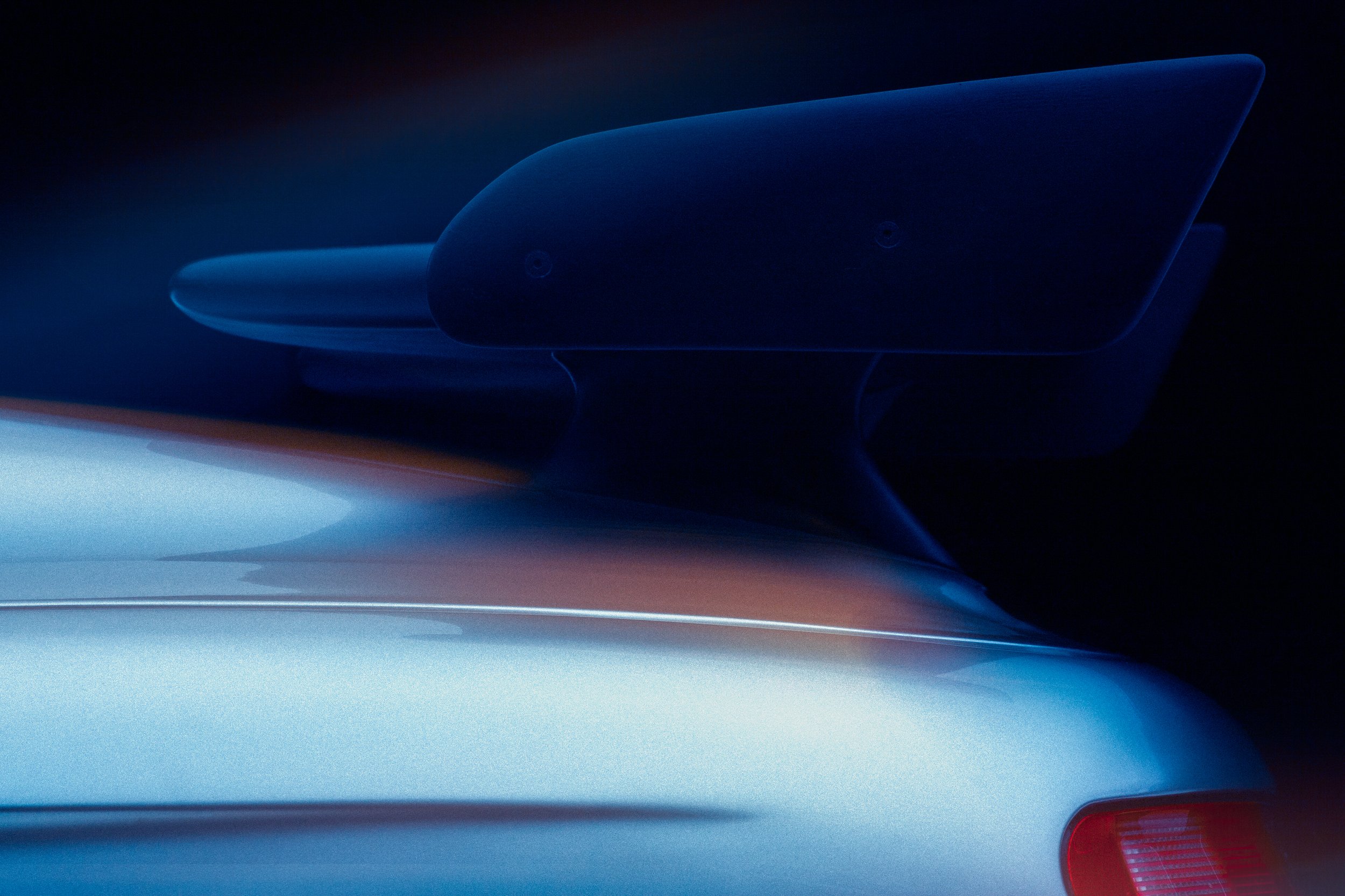 Close-up of the rear spoiler of a silver sports car against a dark background.