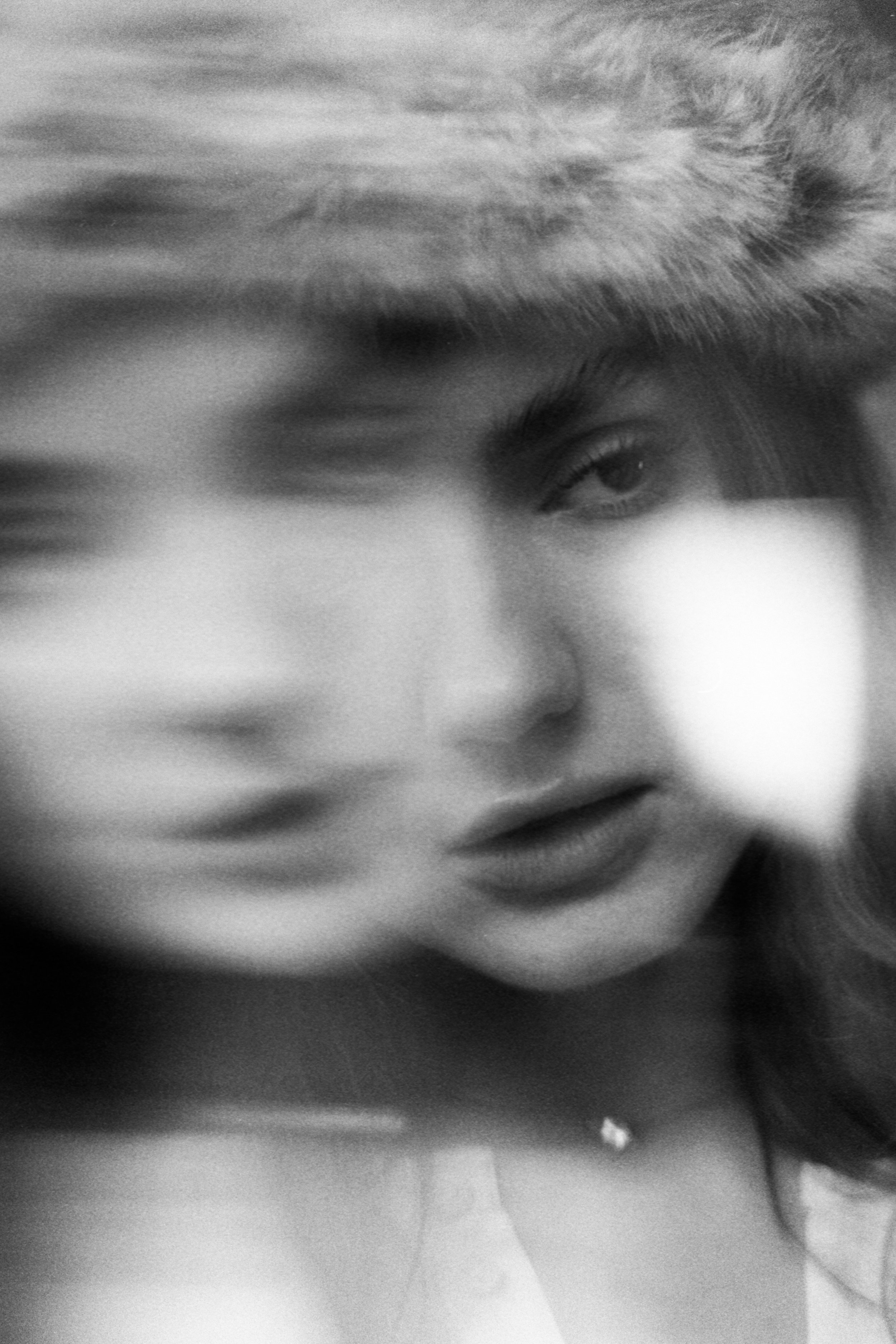 A black and white photograph of a woman's face with hair covering part of her face, one eye visible, and a somewhat blurred, artistic style.