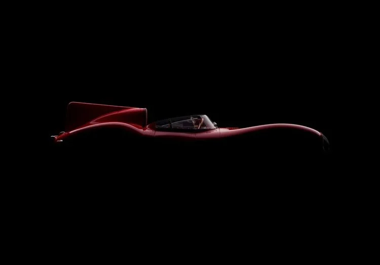 Side view of a sleek, red sports car in a dark setting with minimal lighting highlighting its body shape.