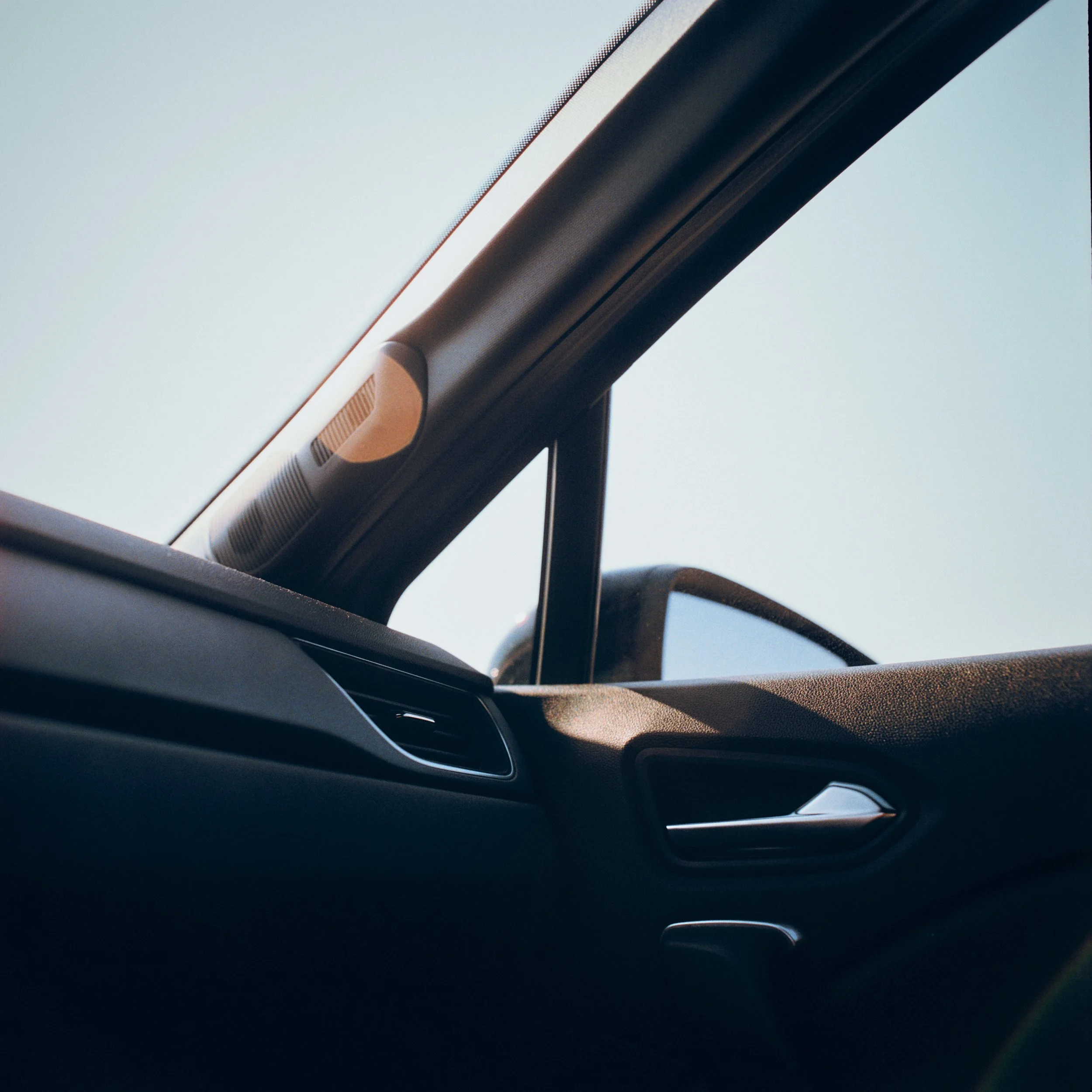 Close-up of a car's rearview mirror and interior, with an external view through the windshield showing a clear sky.