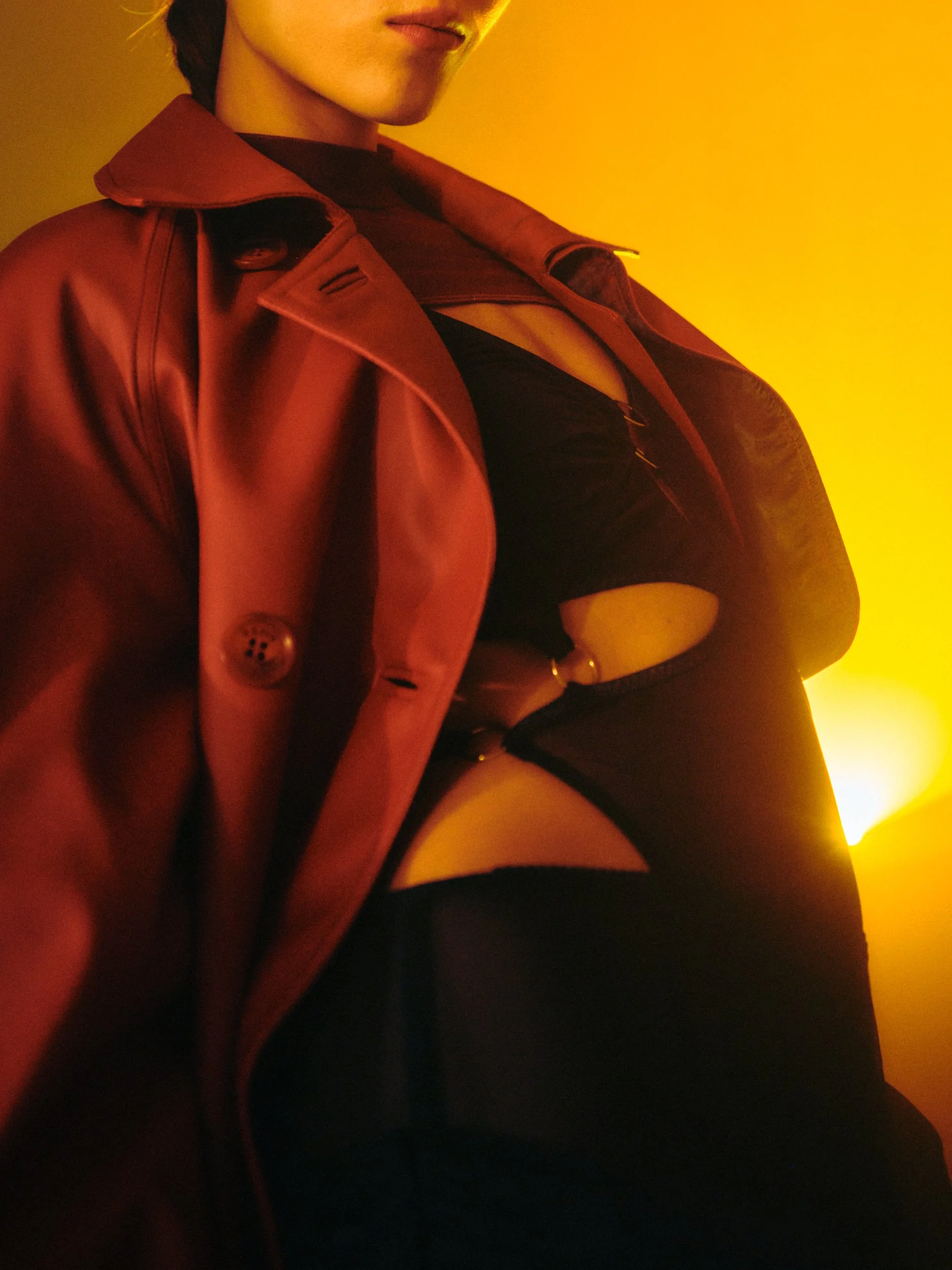 Close-up of a person wearing a red leather jacket and black lingerie, with a yellow background.