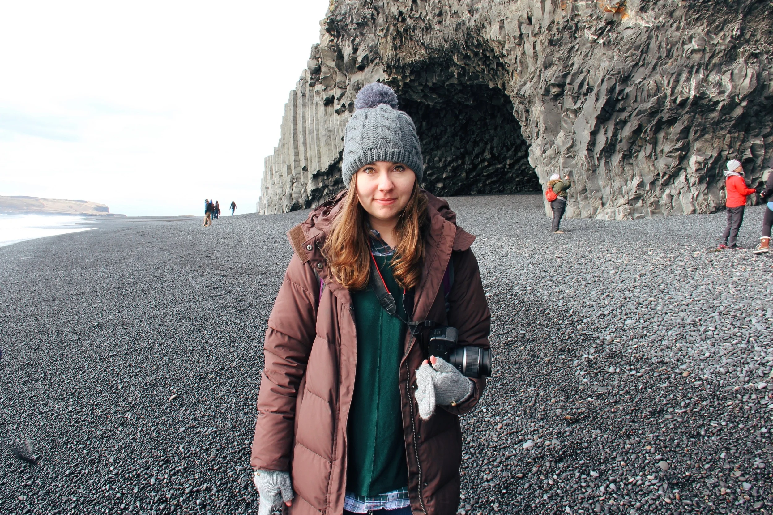 Alice standing on the black sand beaches of Vik, near a basalt cave.