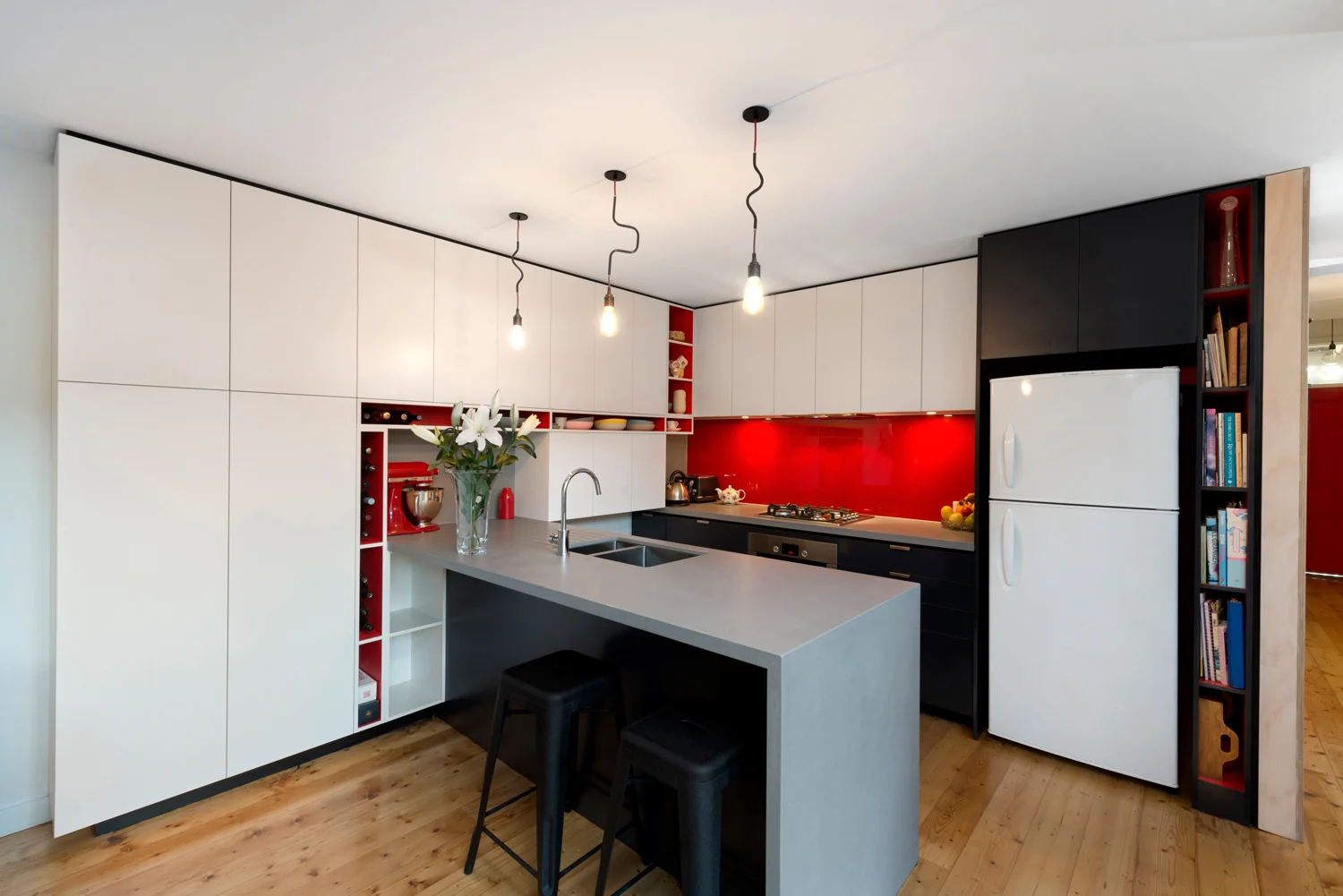 Galley style kitchen with funky lights, red highlights and creative cabinetry.