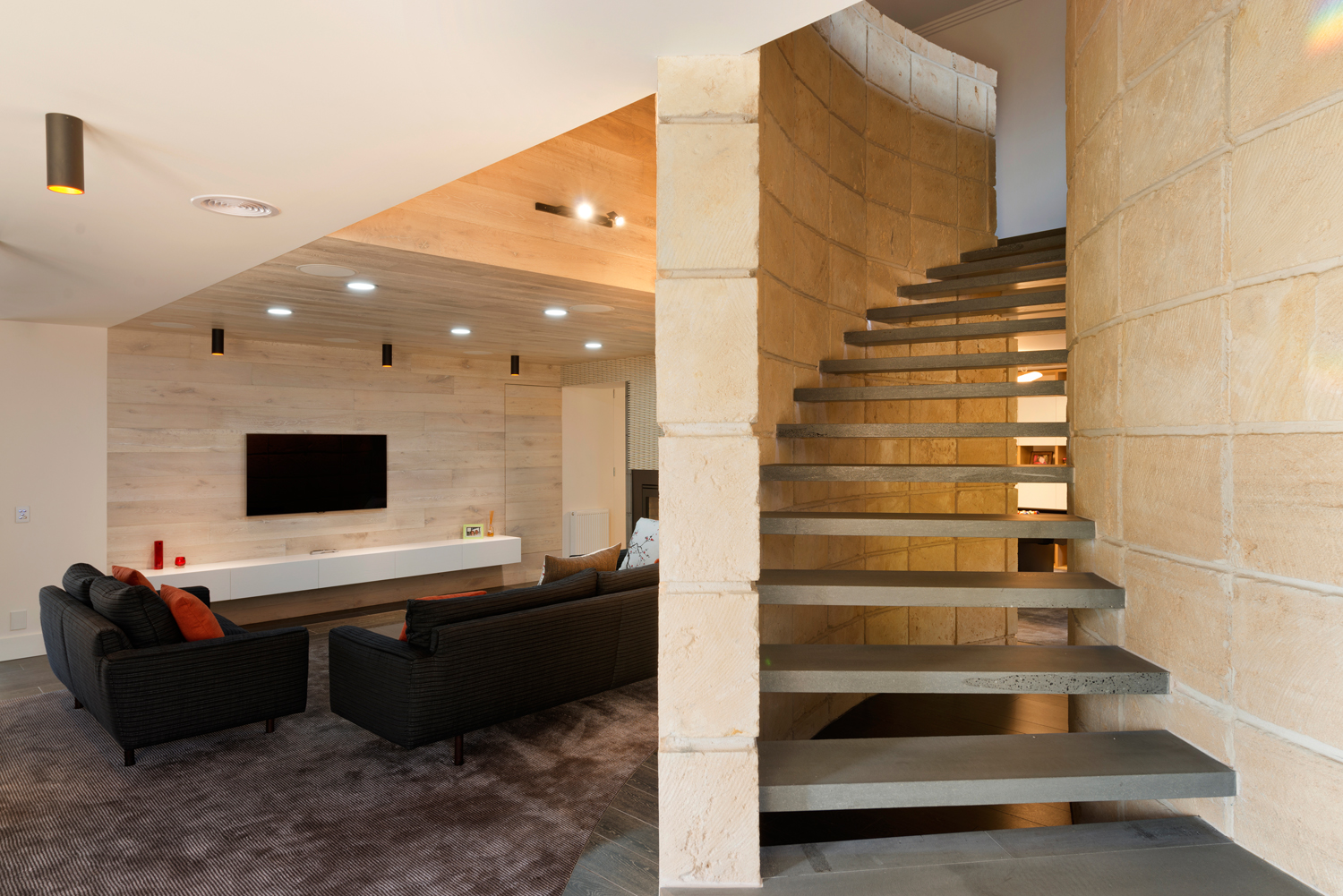Living room with curved sandstone feature wall concealing floating stairs.