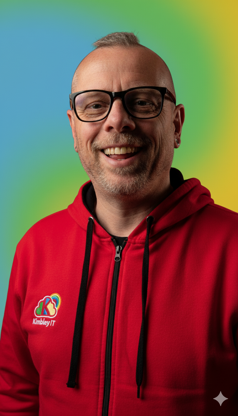 A smiling man with glasses and a goatee wearing a red hoodie with a colorful 'K' logo and 'Kimbley IT' text, standing in front of a rainbow-colored background.