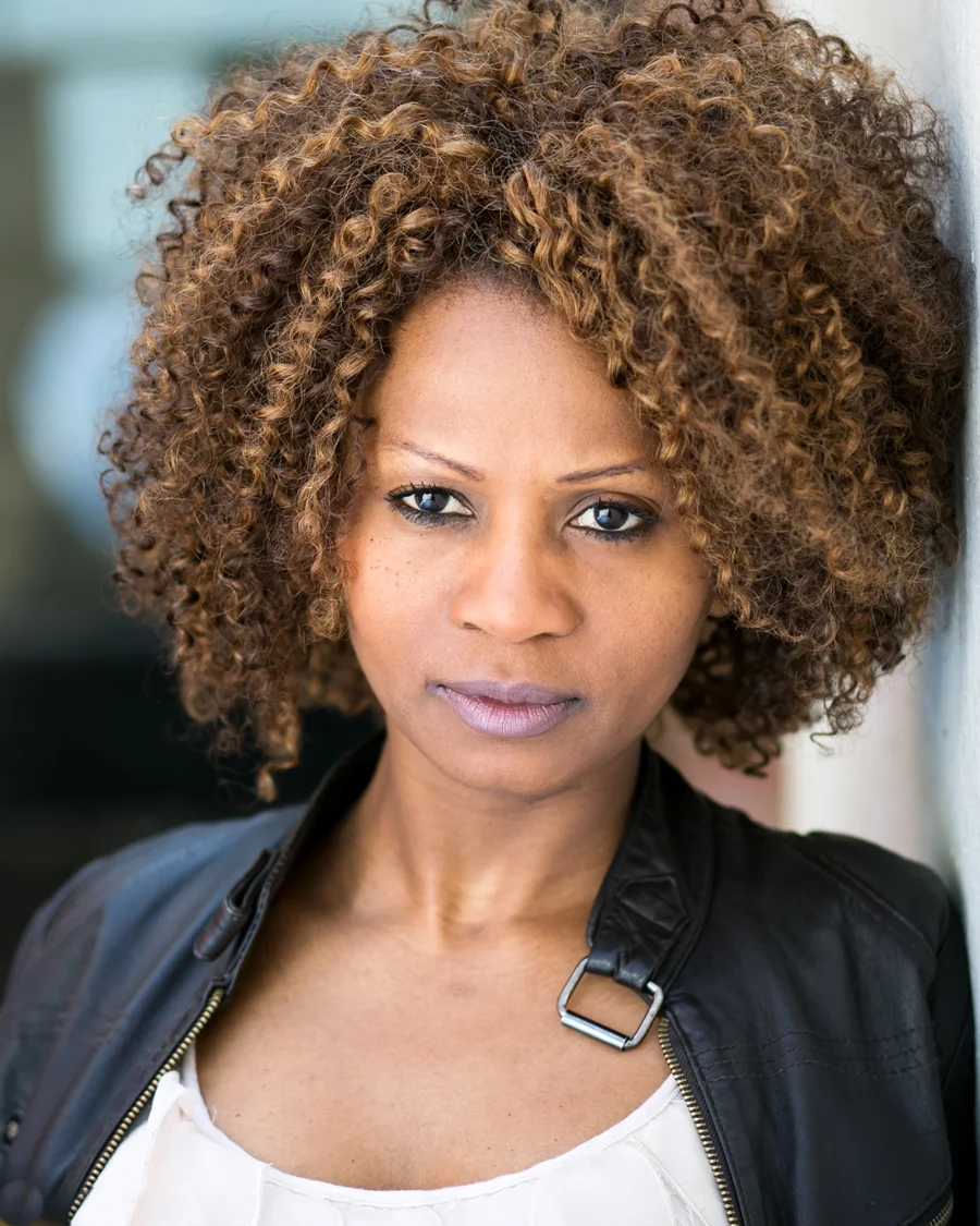 Black actress leaning on a wall with afro wig 