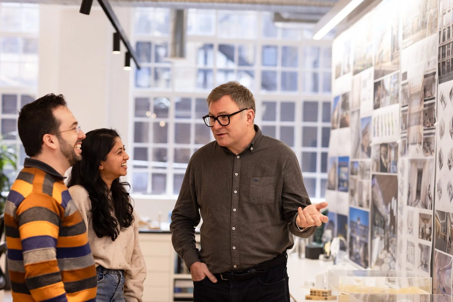  A senior male architect chats with junior colleagues in front of a wall of images 
