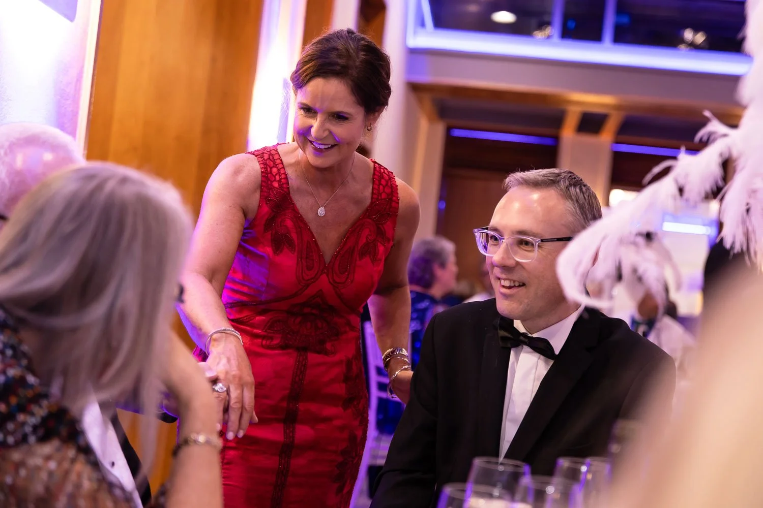  Woman in a red evening dress chatting to dinner guests at a gala dinner party 