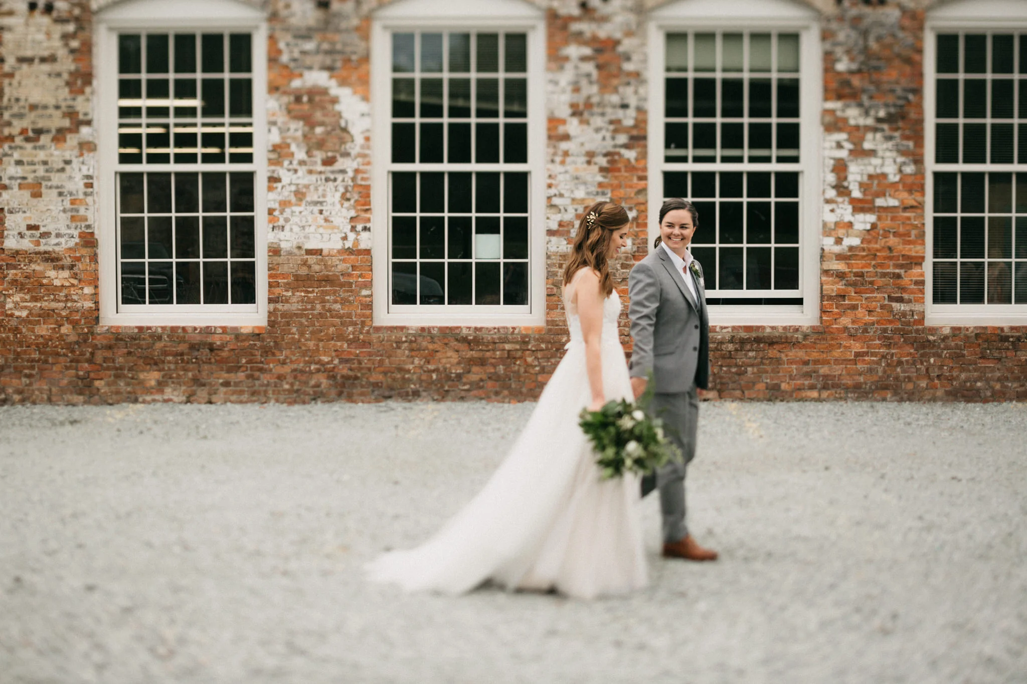Same sex couple walks in front of the warehouse at the Cloth Mill at Eno River in Hillsborough, NC. 