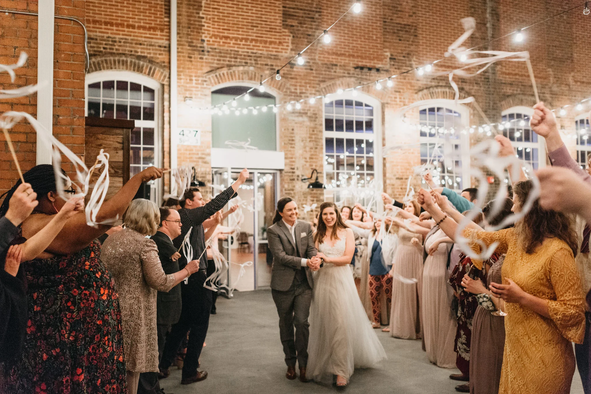 Ribbon send off for newlyweds at the end of their reception with string lights and guests in celebration. 