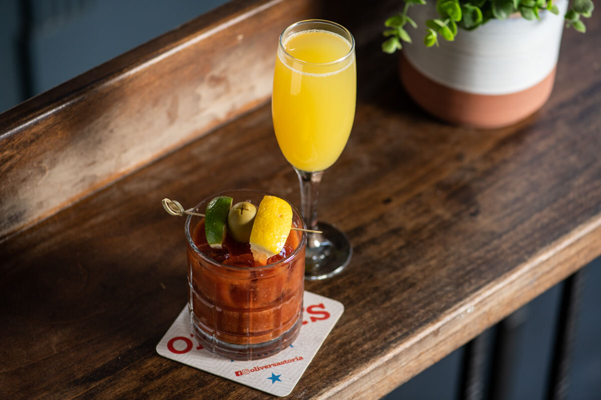 A bloody mary cocktail on a cocktail napkin next to a flute of mimosa